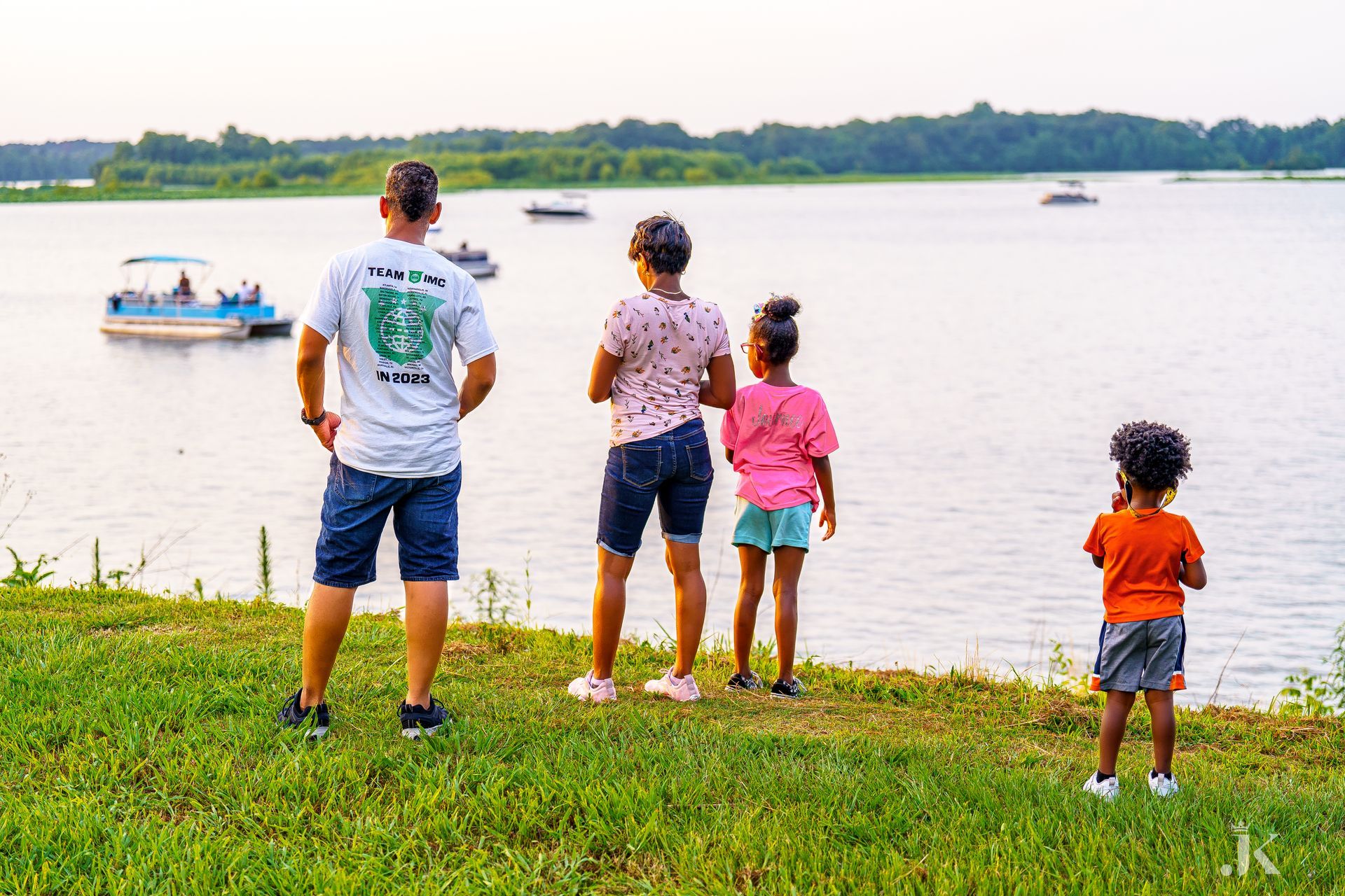 A family is standing on the shore of a lake looking at boats.