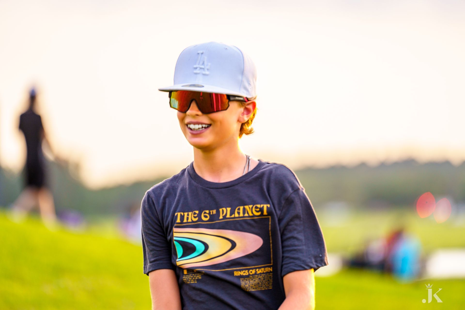 A young boy wearing sunglasses and a hat is sitting in a field.