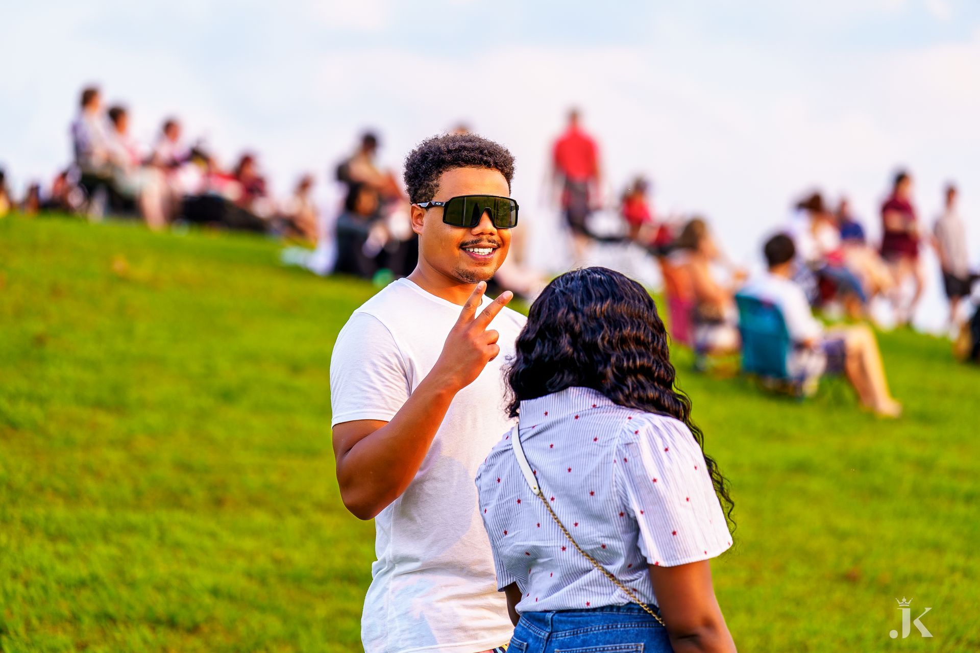 A man and a woman are standing on top of a grassy hill.