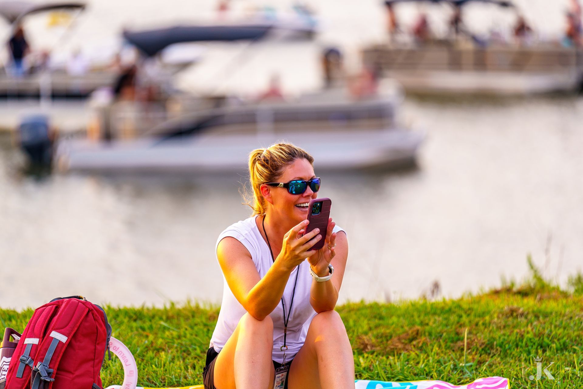 A woman is sitting on the grass looking at her cell phone.