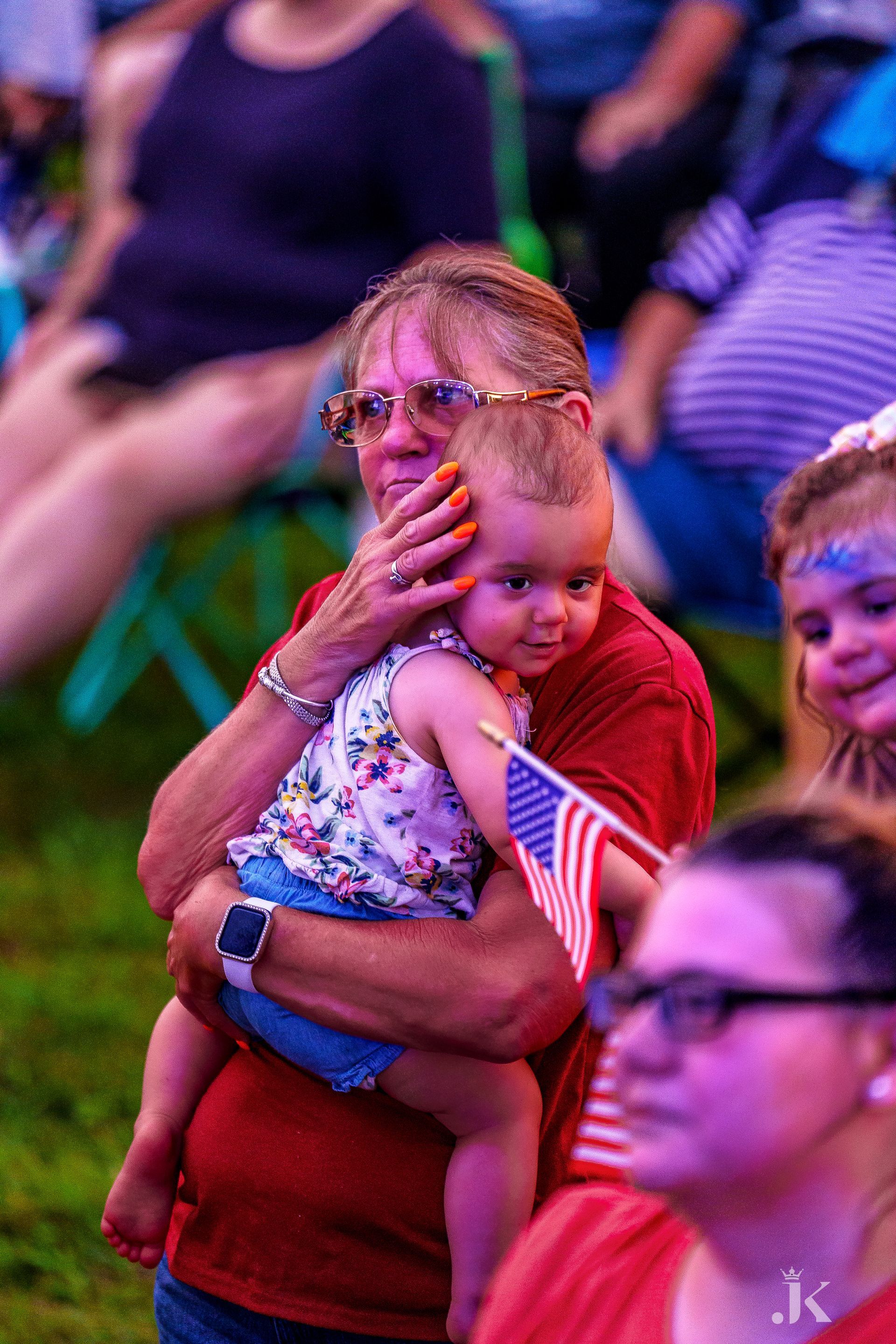 A woman is holding a baby in her arms while sitting in a crowd of people.