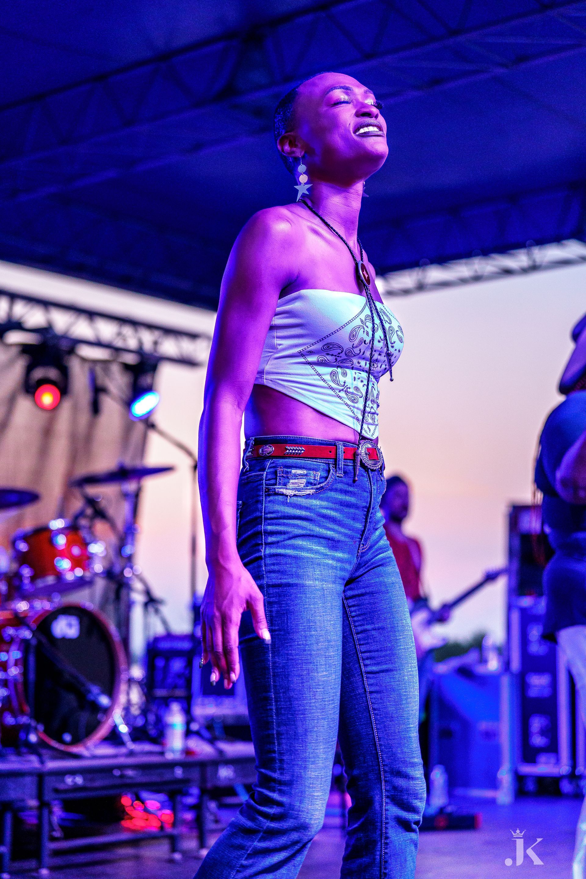 A woman is standing on a stage in front of a drum set.