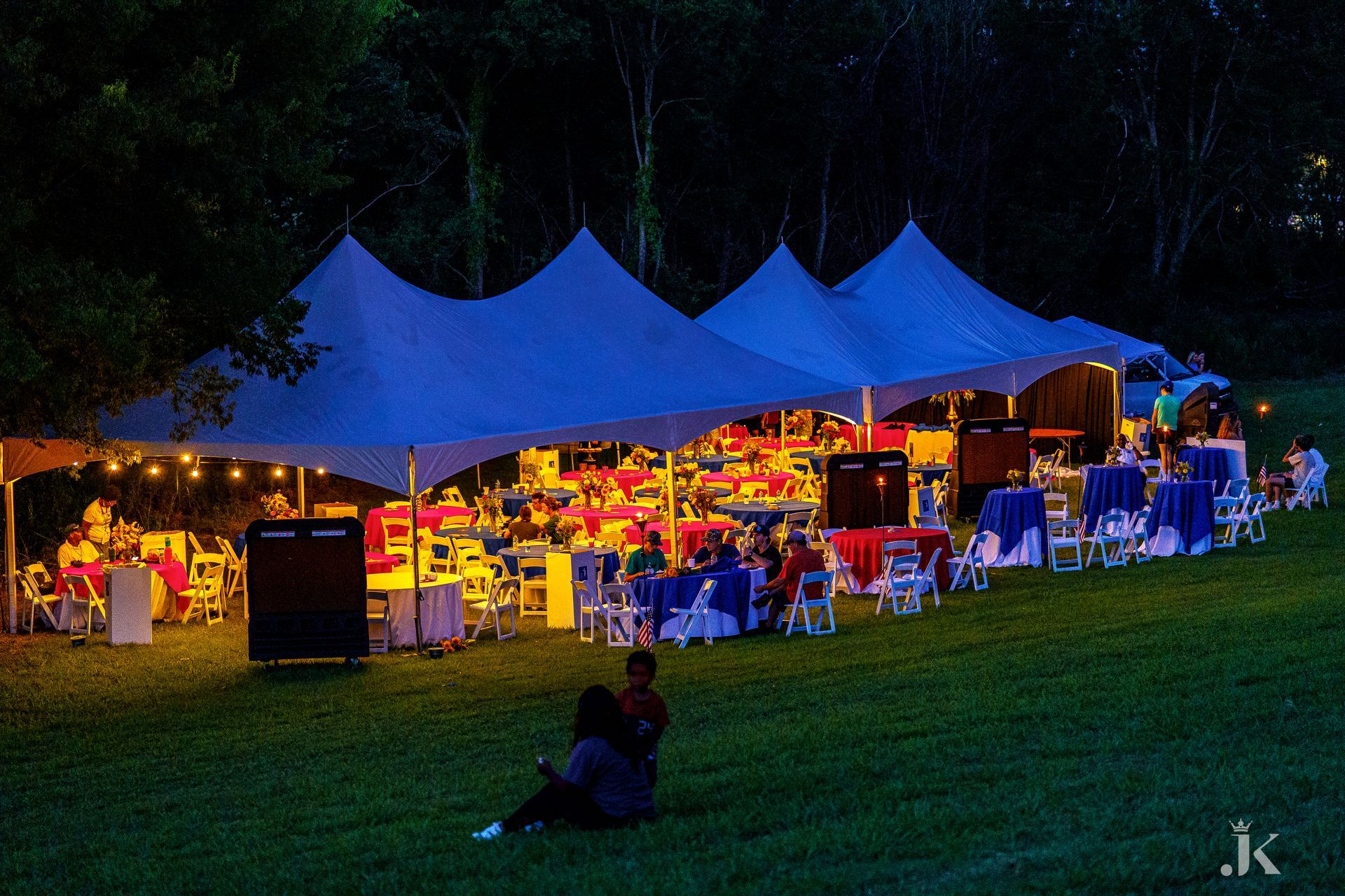 A group of people are sitting under a tent at night.