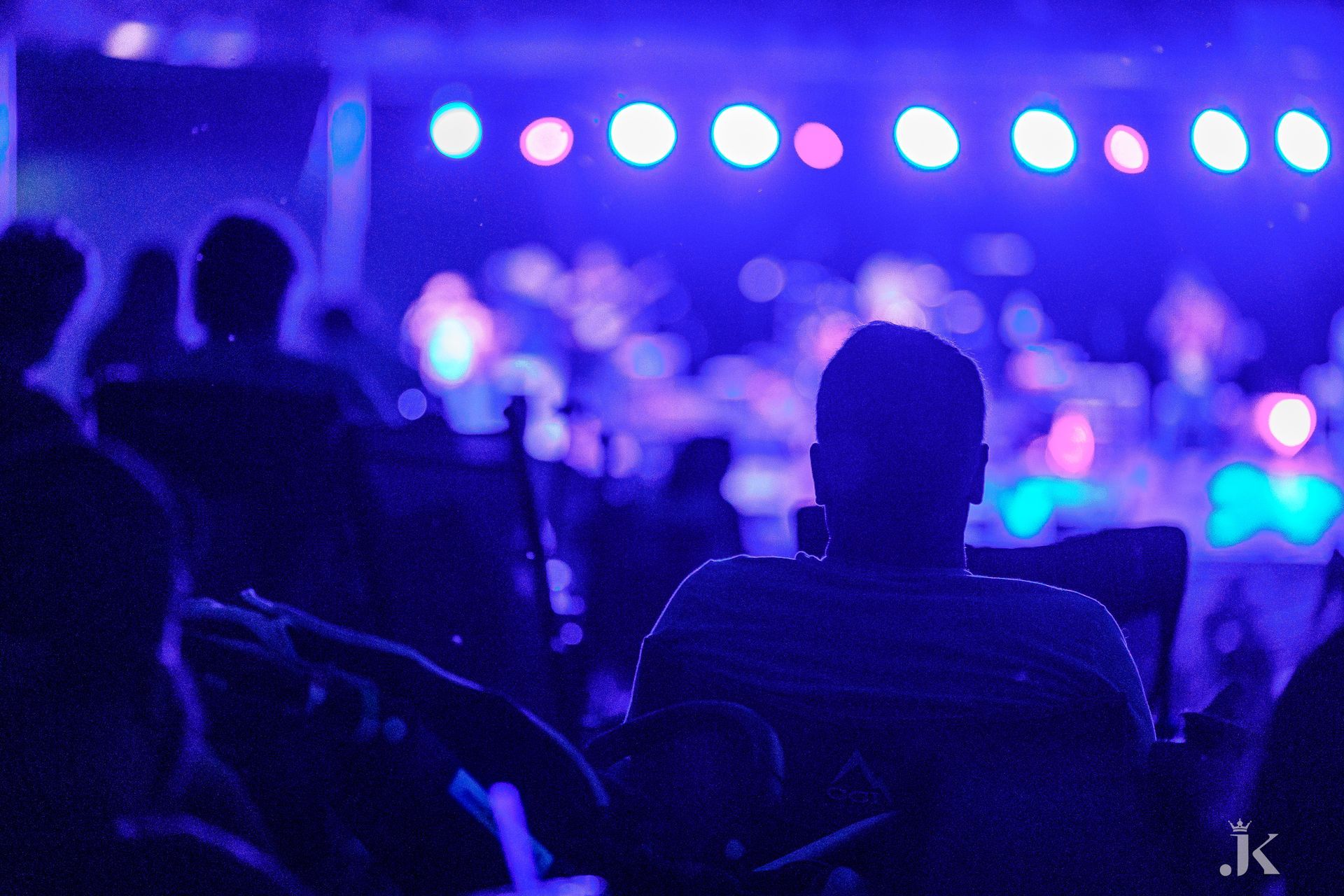 A group of people are sitting in front of a stage with blue lights.