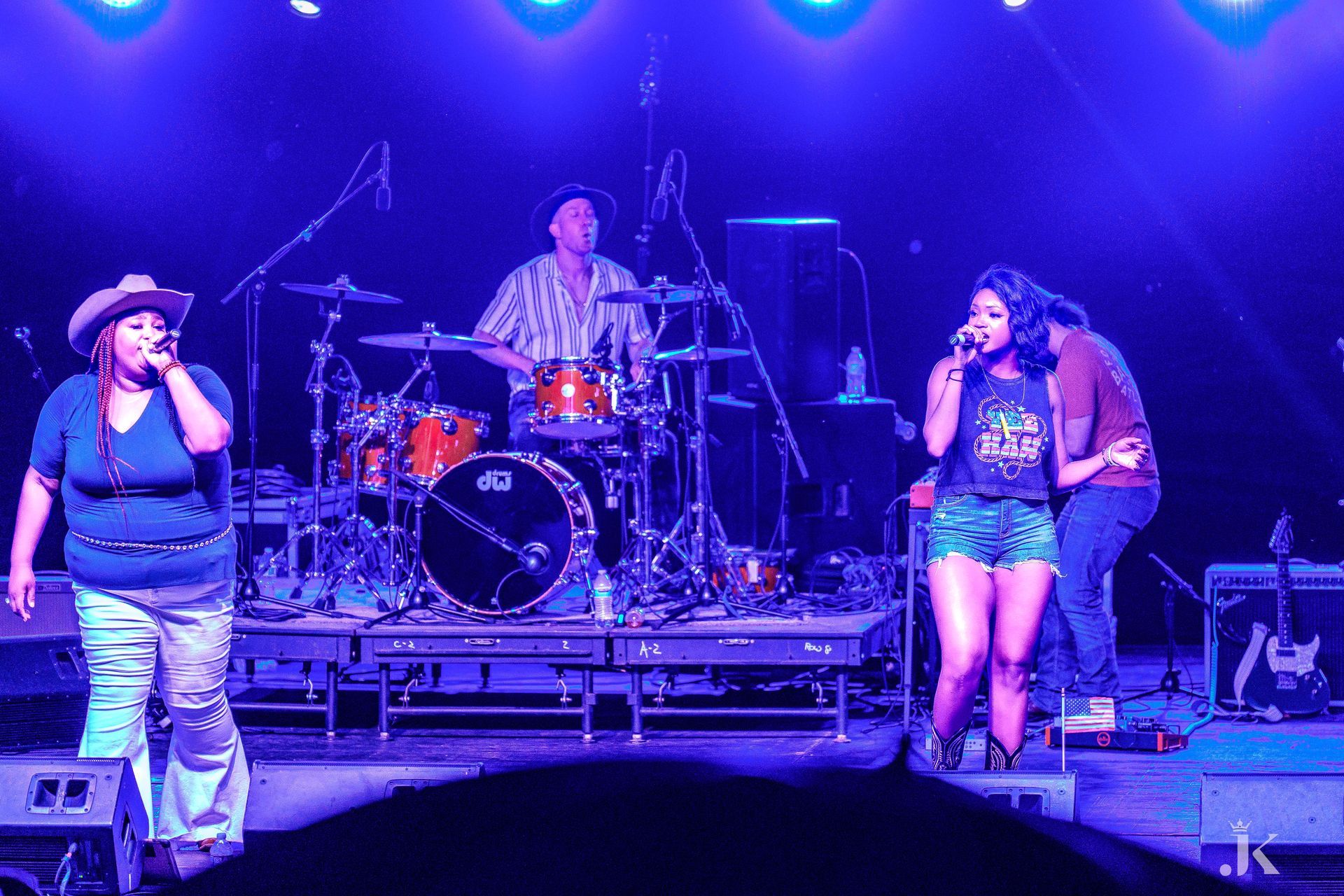 A group of people singing on a stage with a drummer in the background