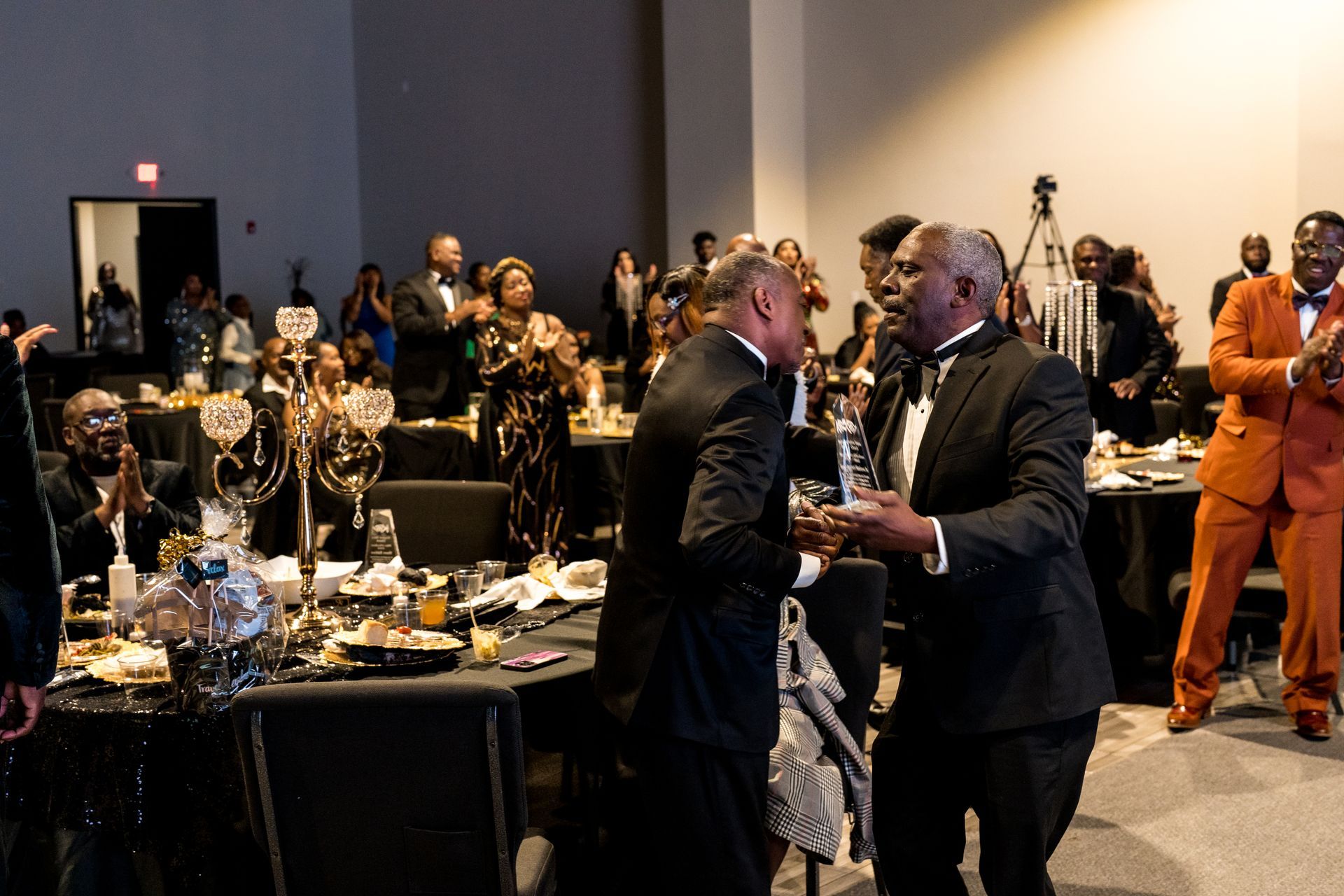 A group of men in suits are dancing in a room with people sitting at tables.