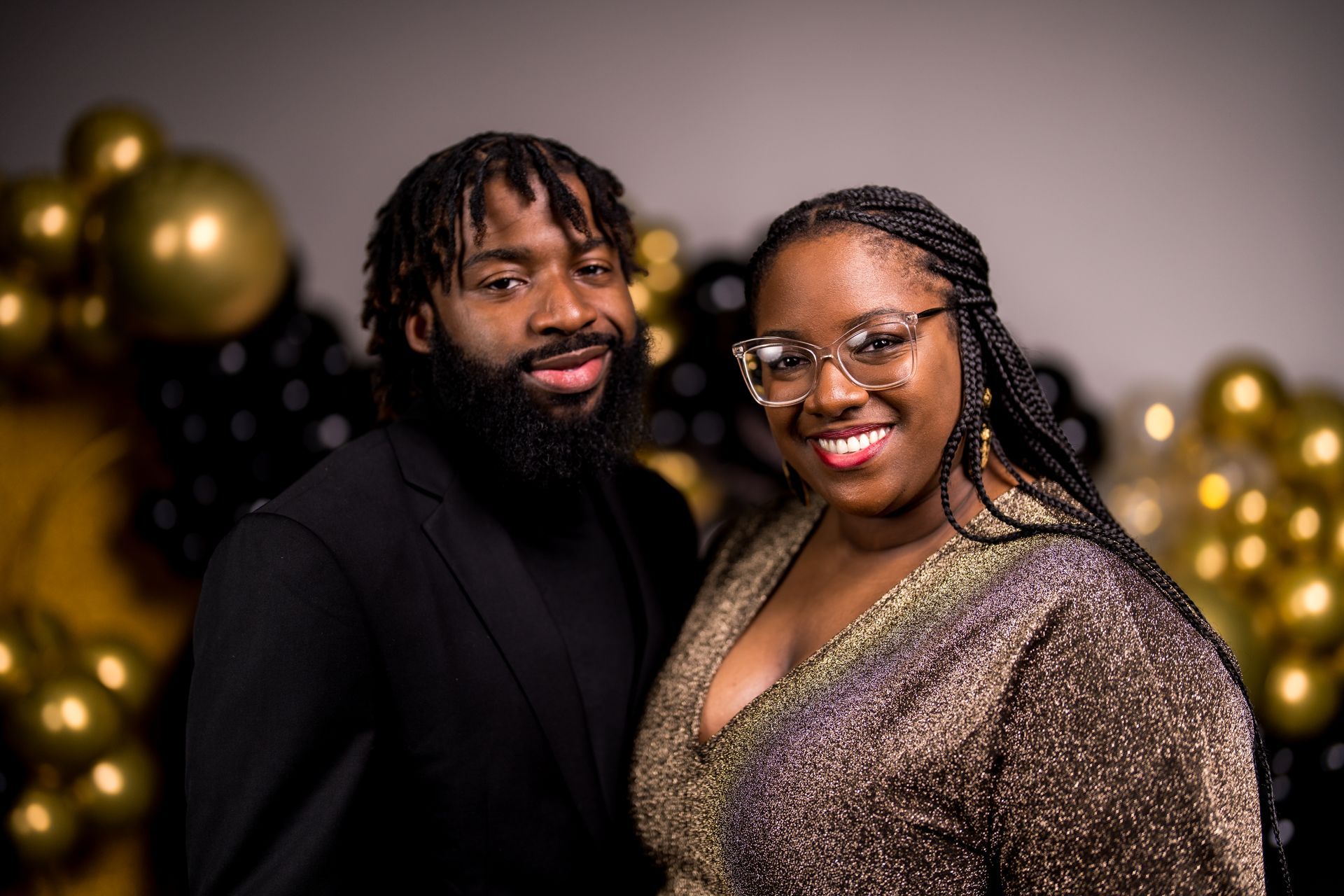 A man and a woman are posing for a picture in front of balloons.