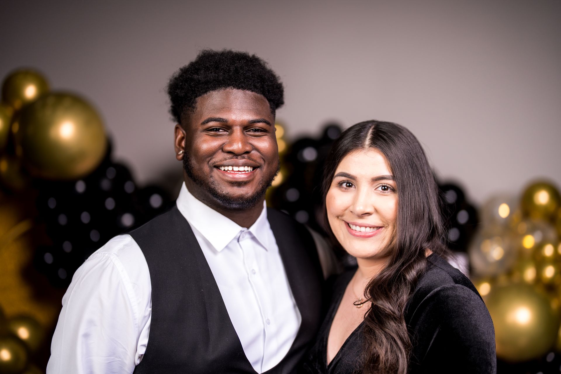 A man and a woman are posing for a picture in front of balloons.