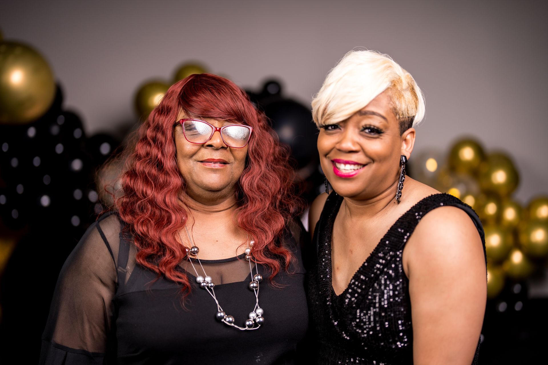 Two women are posing for a picture in front of balloons.