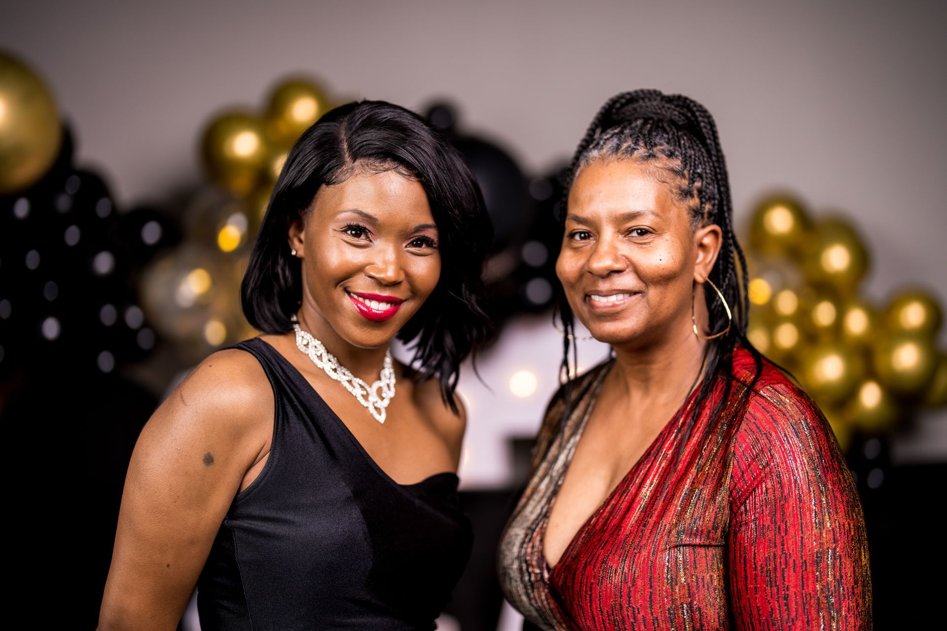 Two women are posing for a picture together in front of balloons.