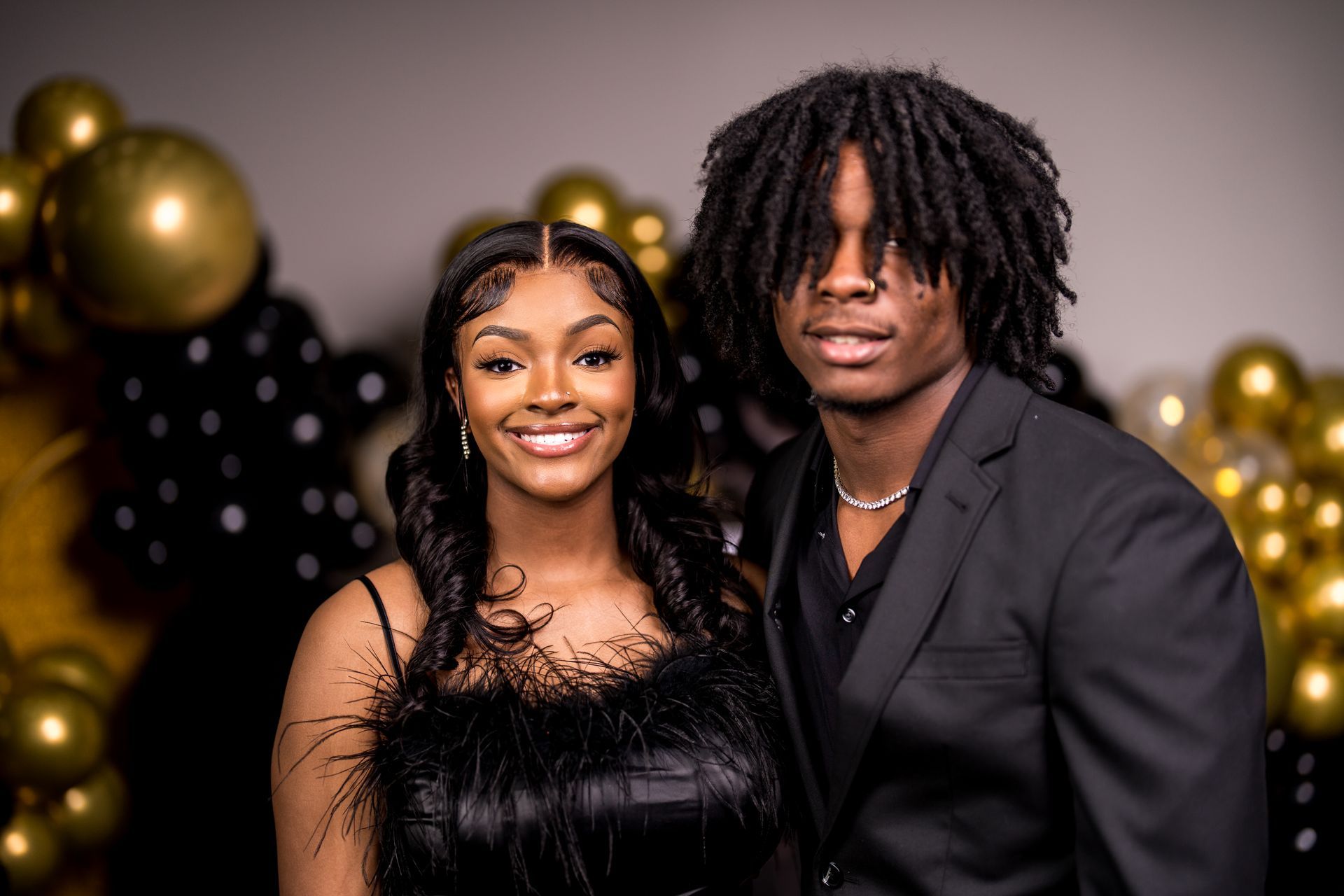 A man and a woman are posing for a picture in front of balloons.