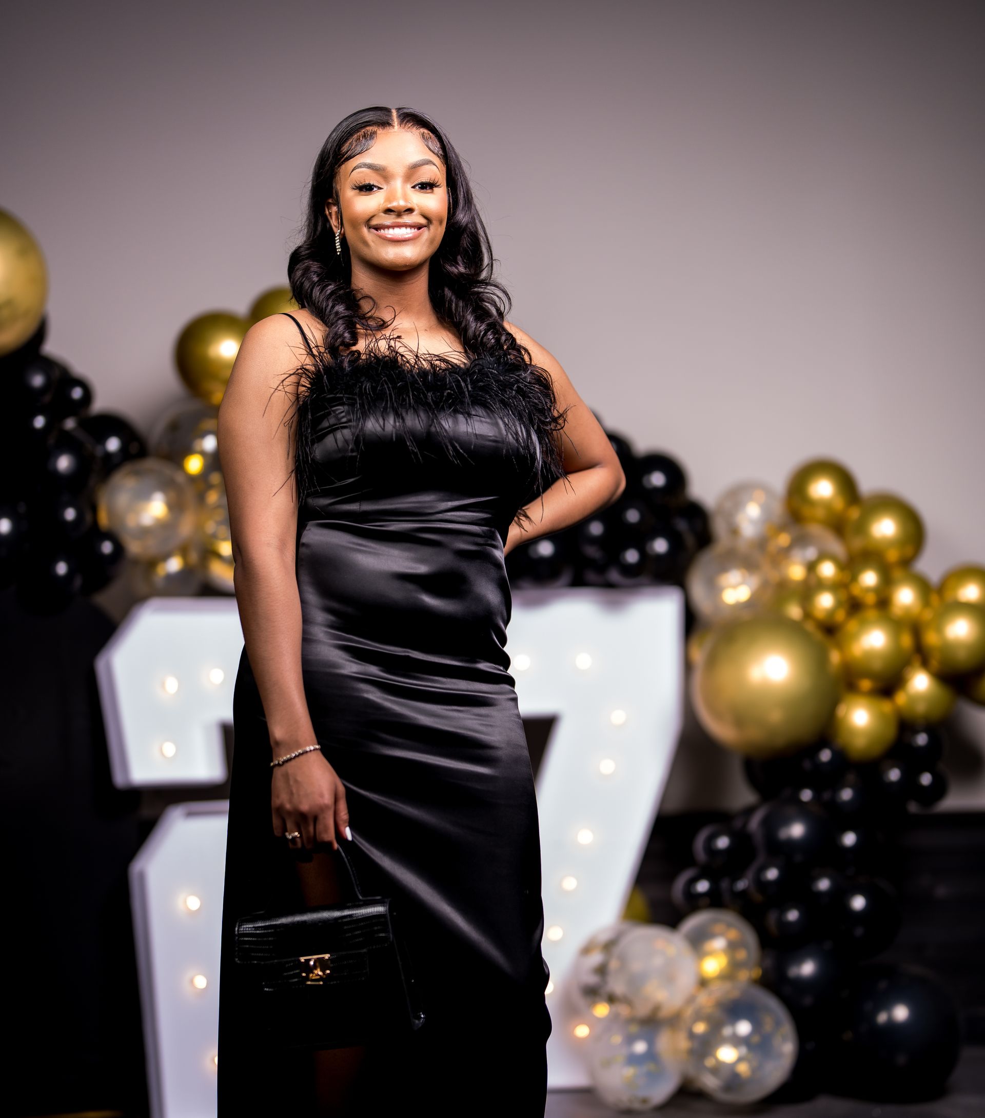 A woman in a black dress is standing in front of balloons and a number 7.