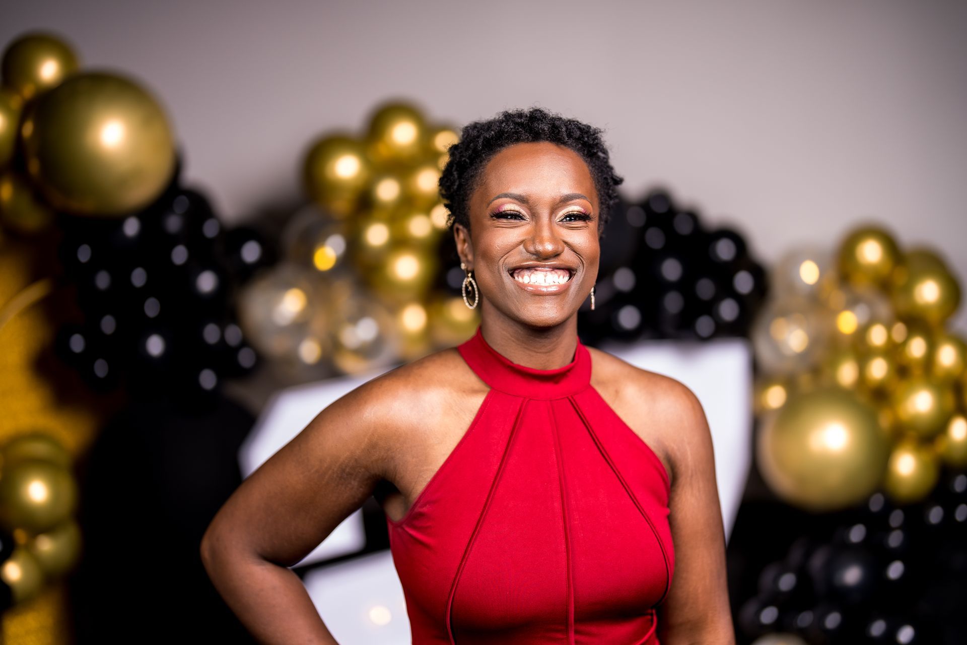 A woman in a red dress is smiling in front of balloons.