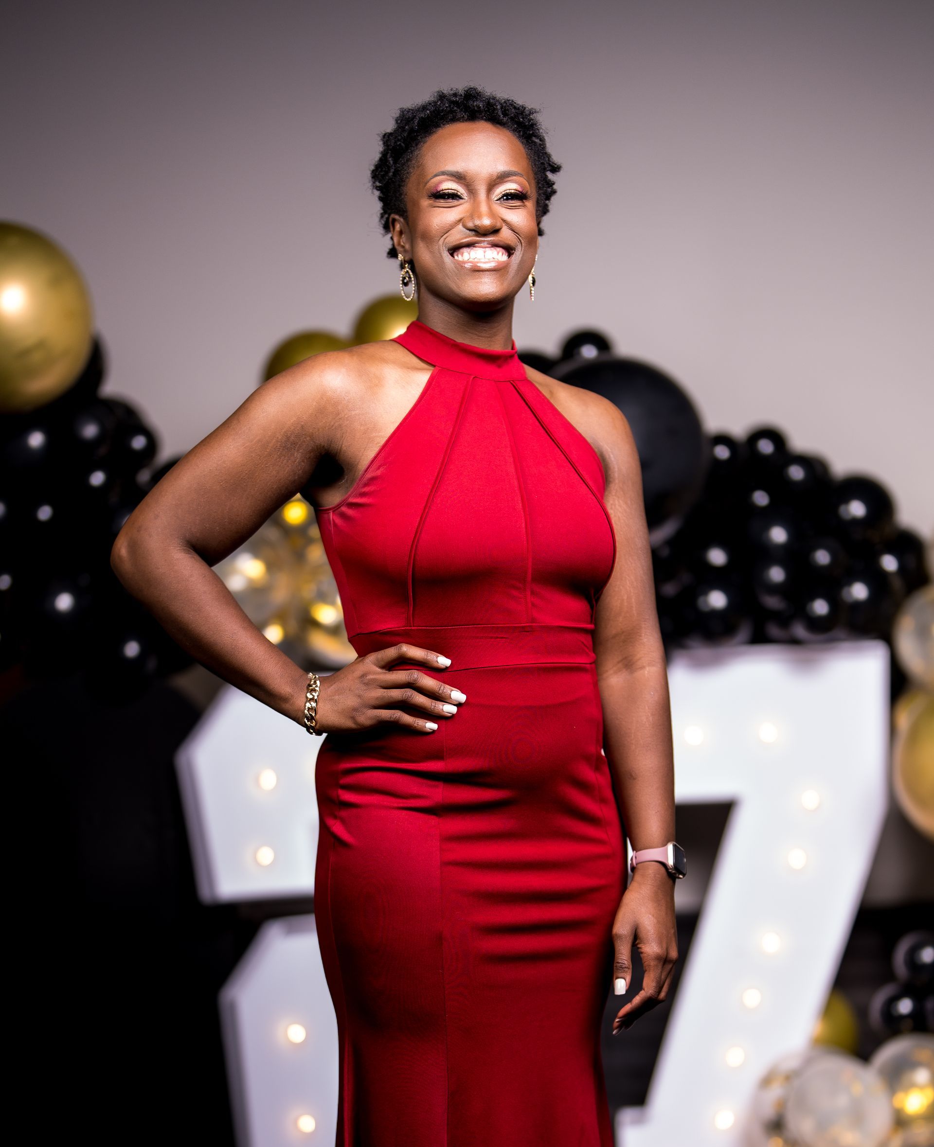 A woman in a red dress is standing in front of balloons.