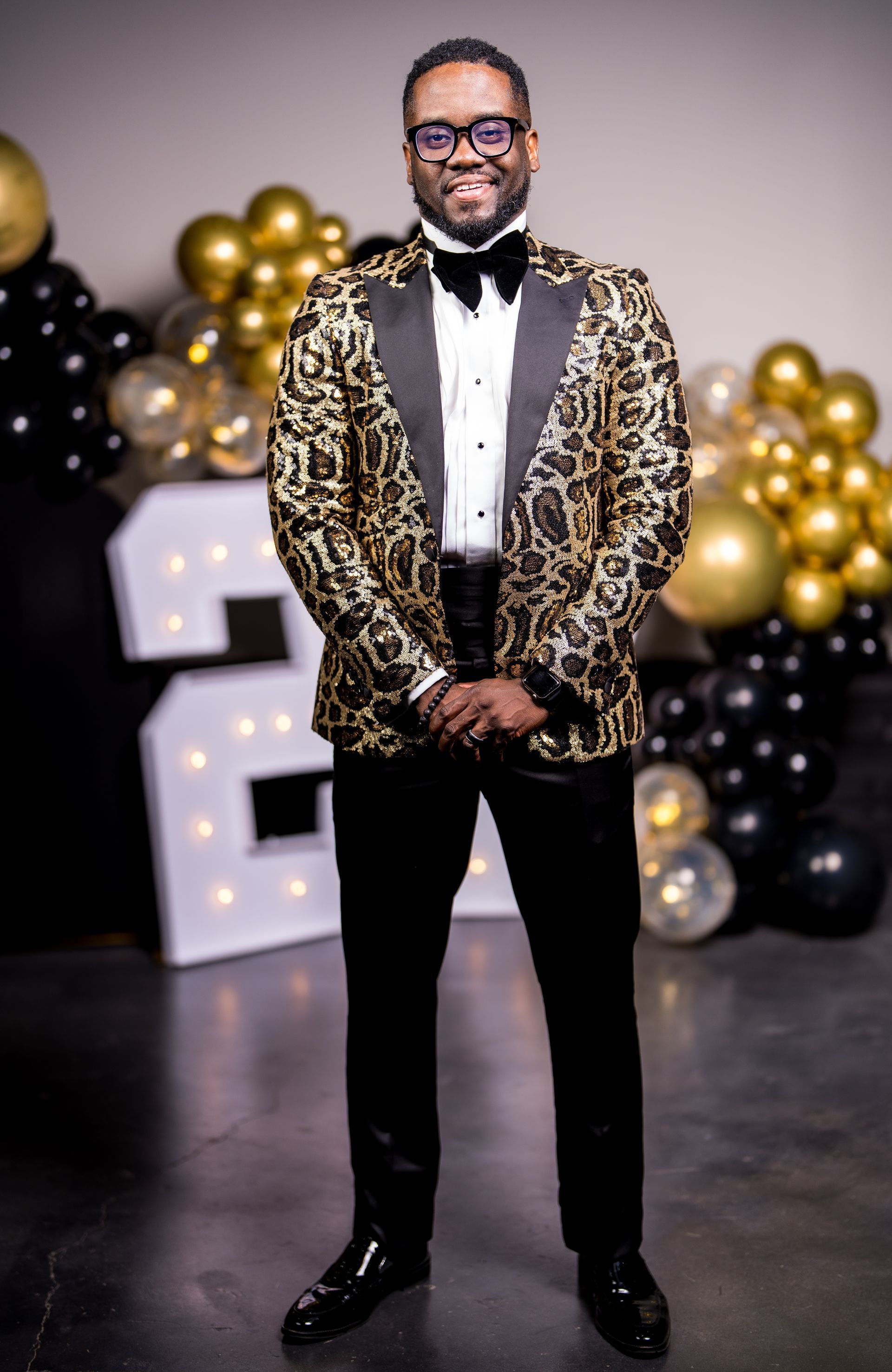 A man in a tuxedo and bow tie is standing in front of balloons.