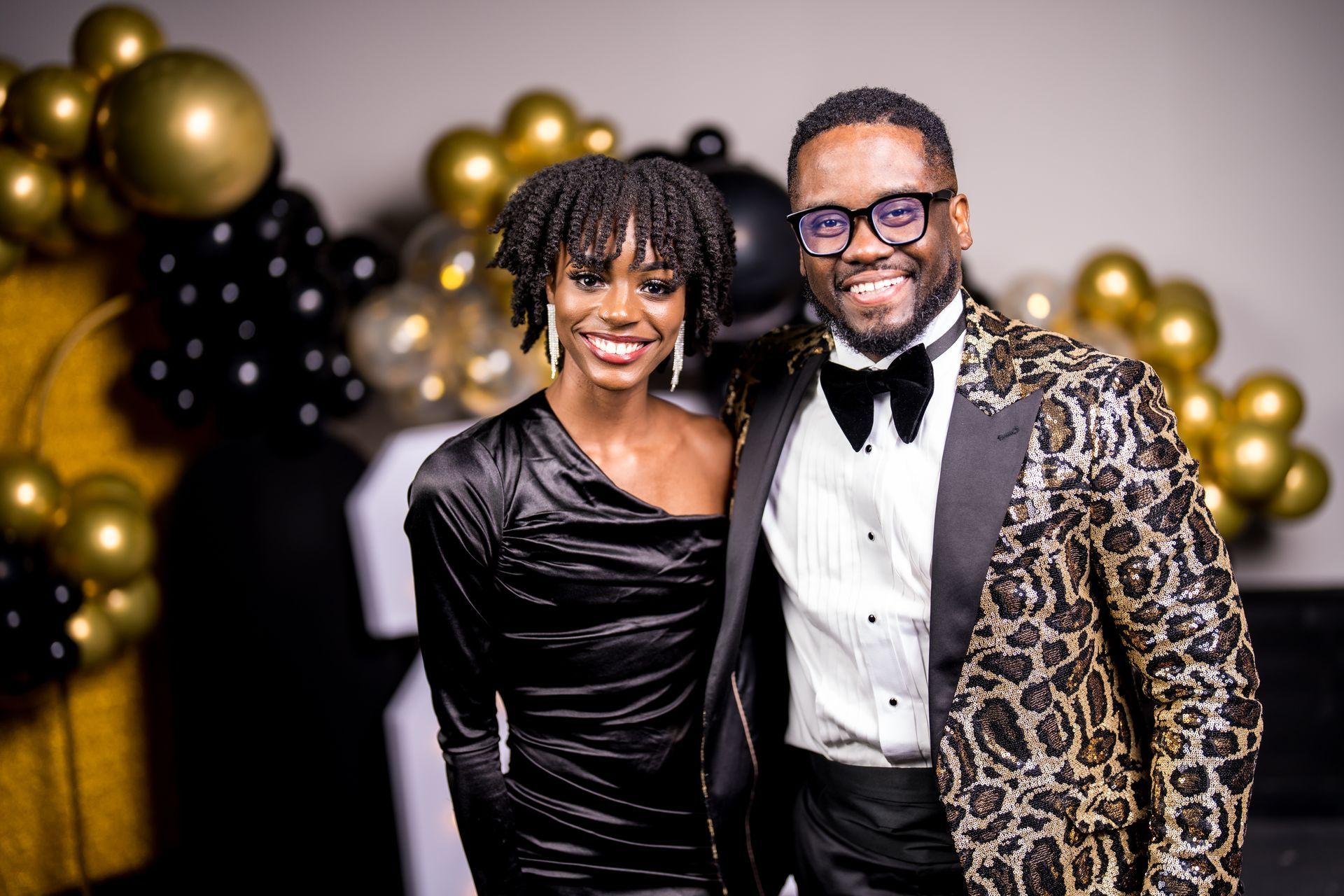 A man and a woman are posing for a picture in front of balloons.