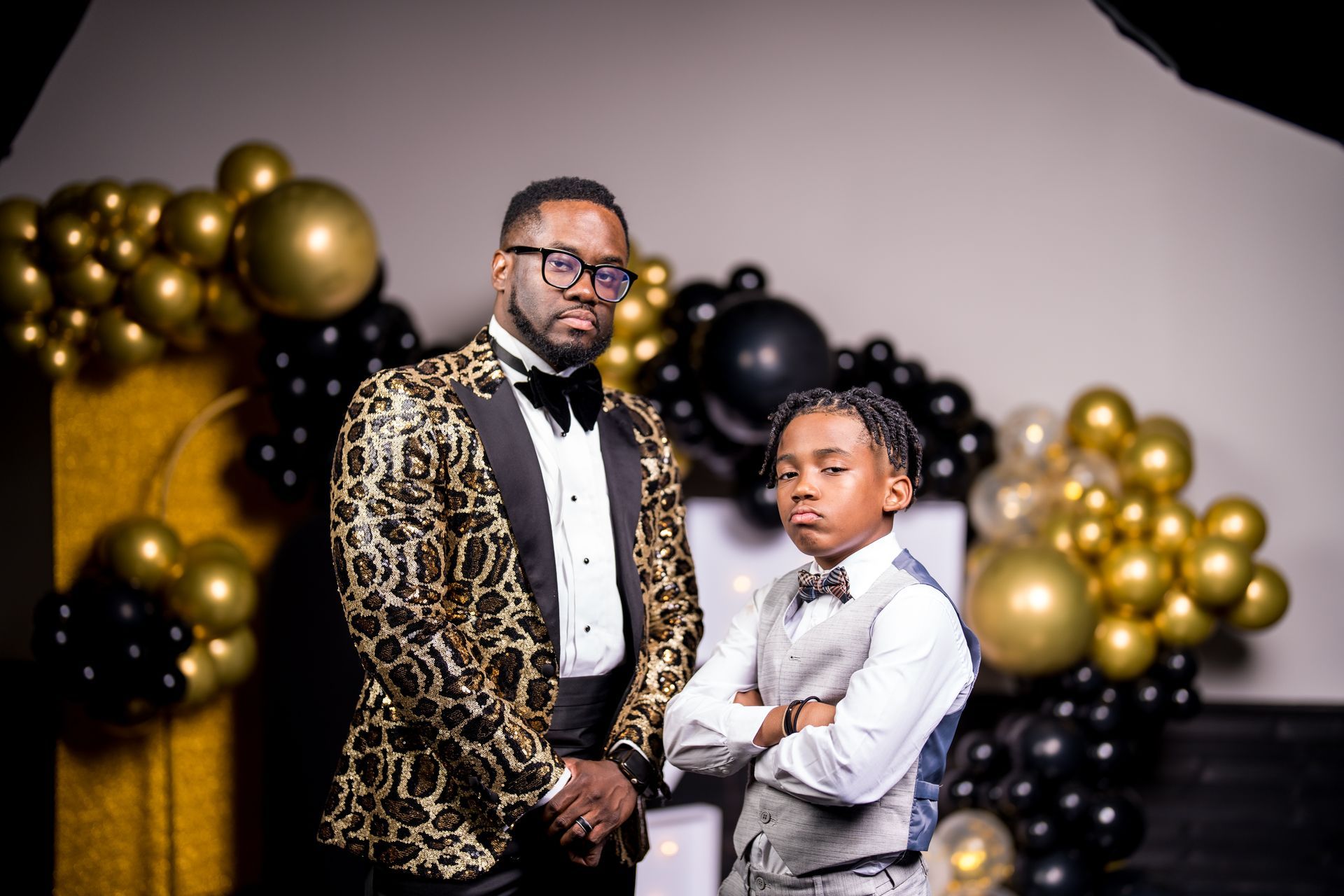 A man and a boy are standing next to each other in front of balloons.