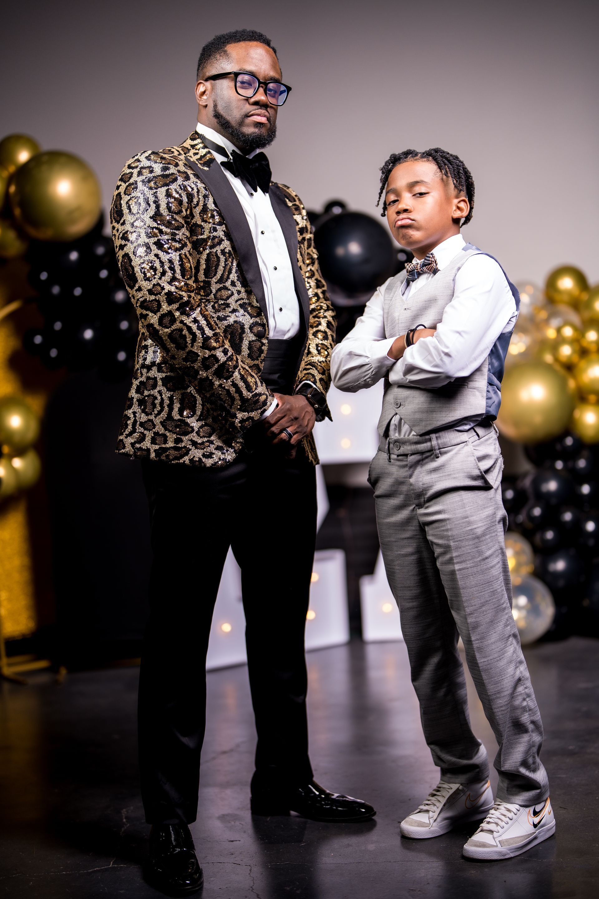 A man and a boy are standing next to each other in front of balloons.