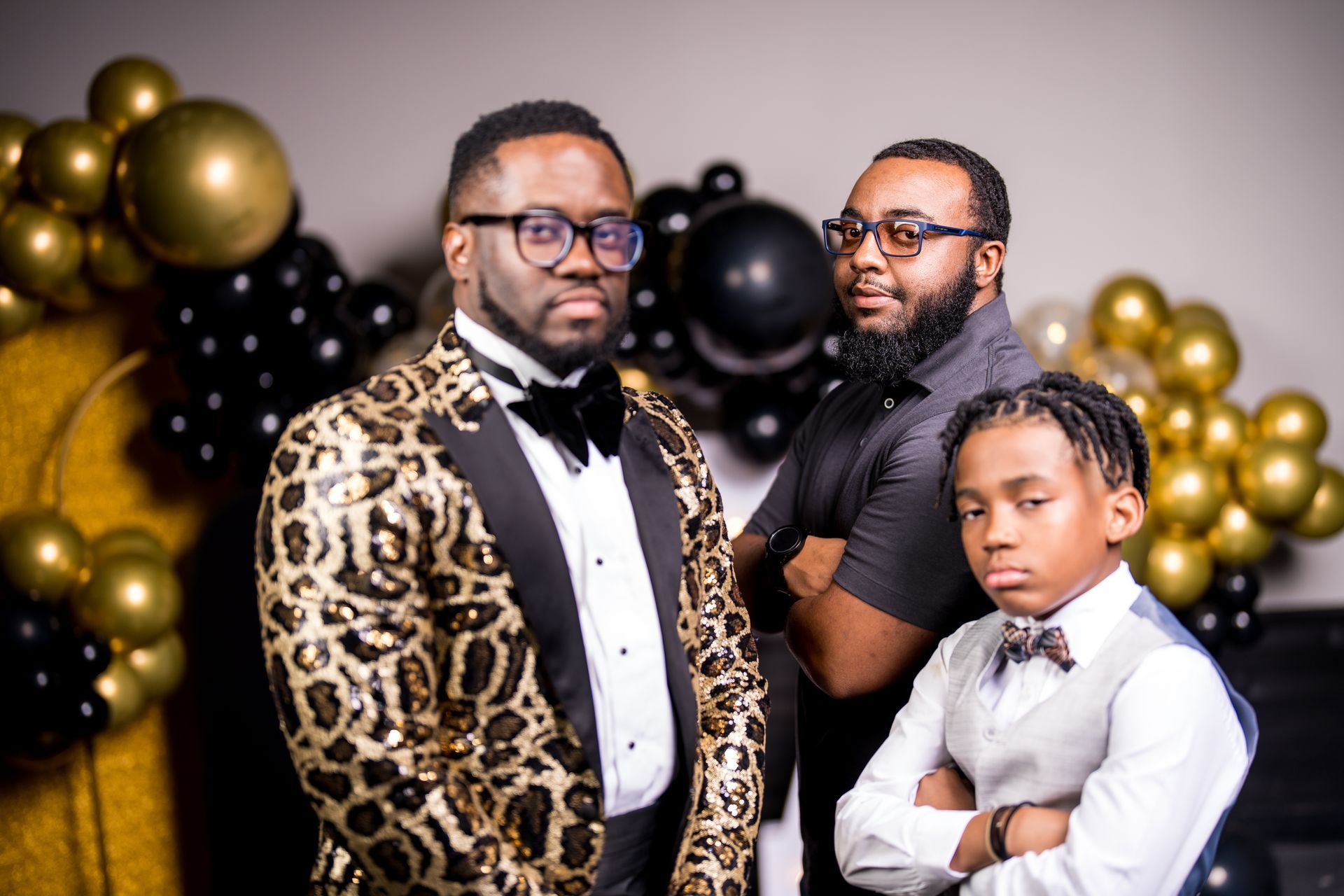 Three men in tuxedos and bow ties are posing for a picture in front of balloons.