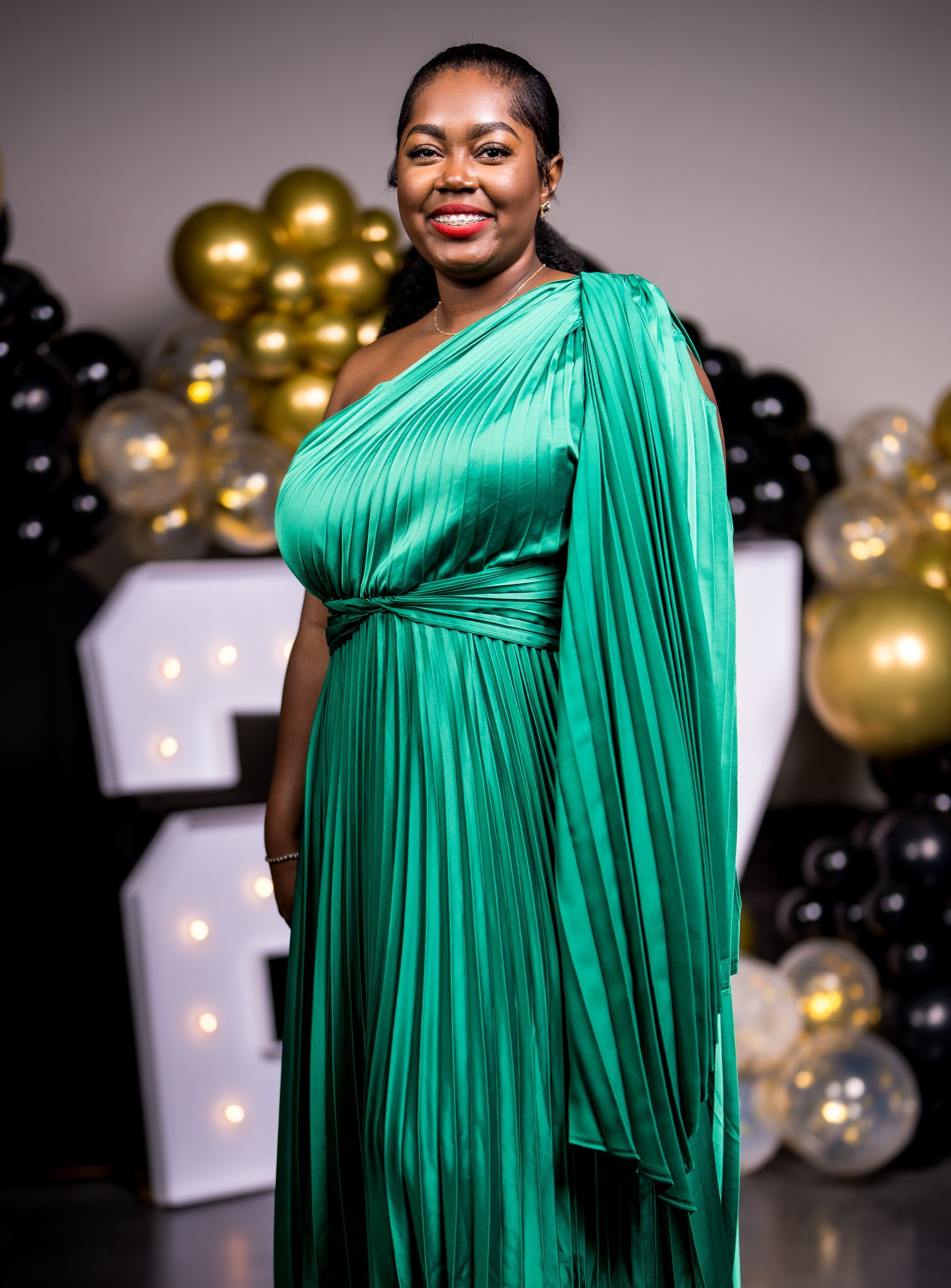 A woman in a green dress is standing in front of balloons.