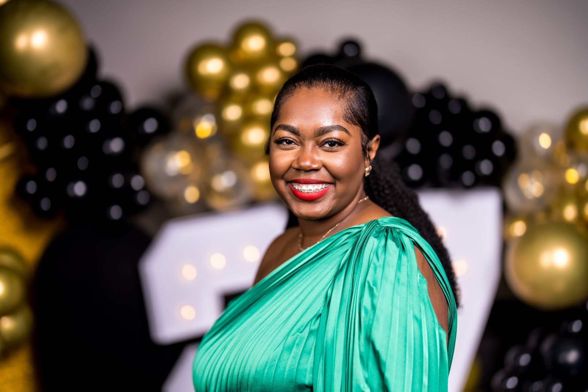 A woman in a green dress is smiling in front of balloons.