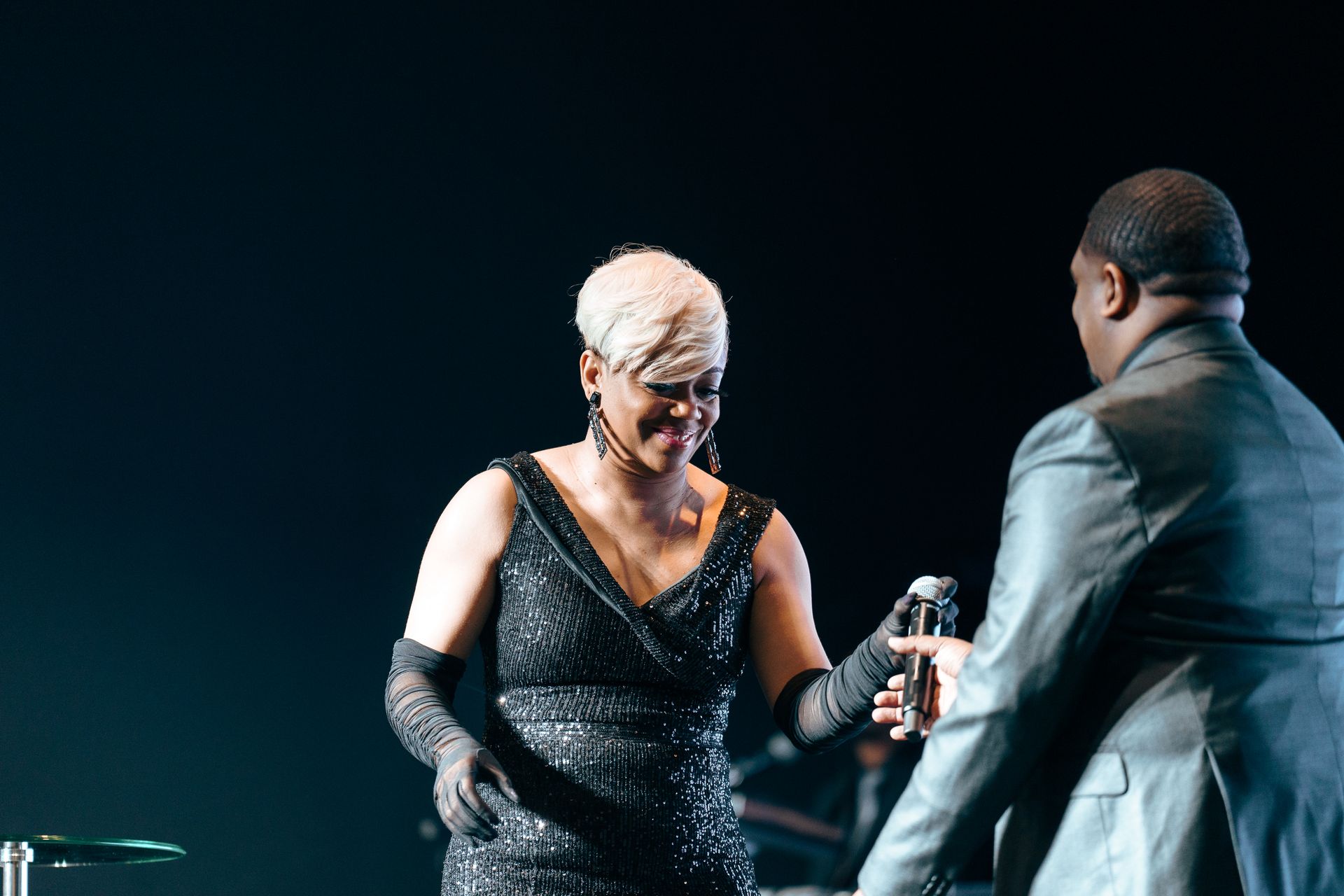 A woman in a black dress is standing next to a man in a suit on a stage holding a microphone.