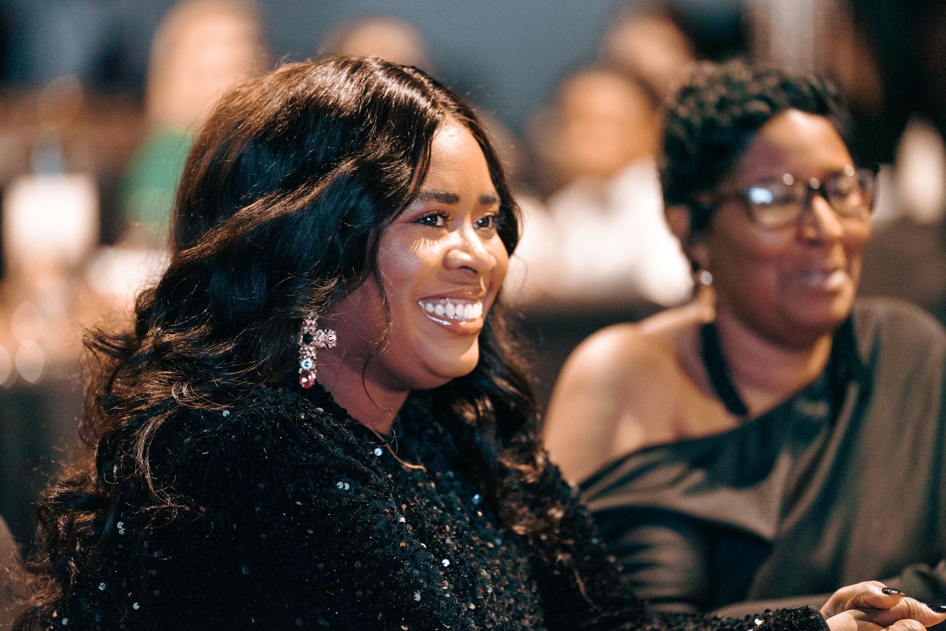 A woman in a black dress is smiling while sitting next to another woman.