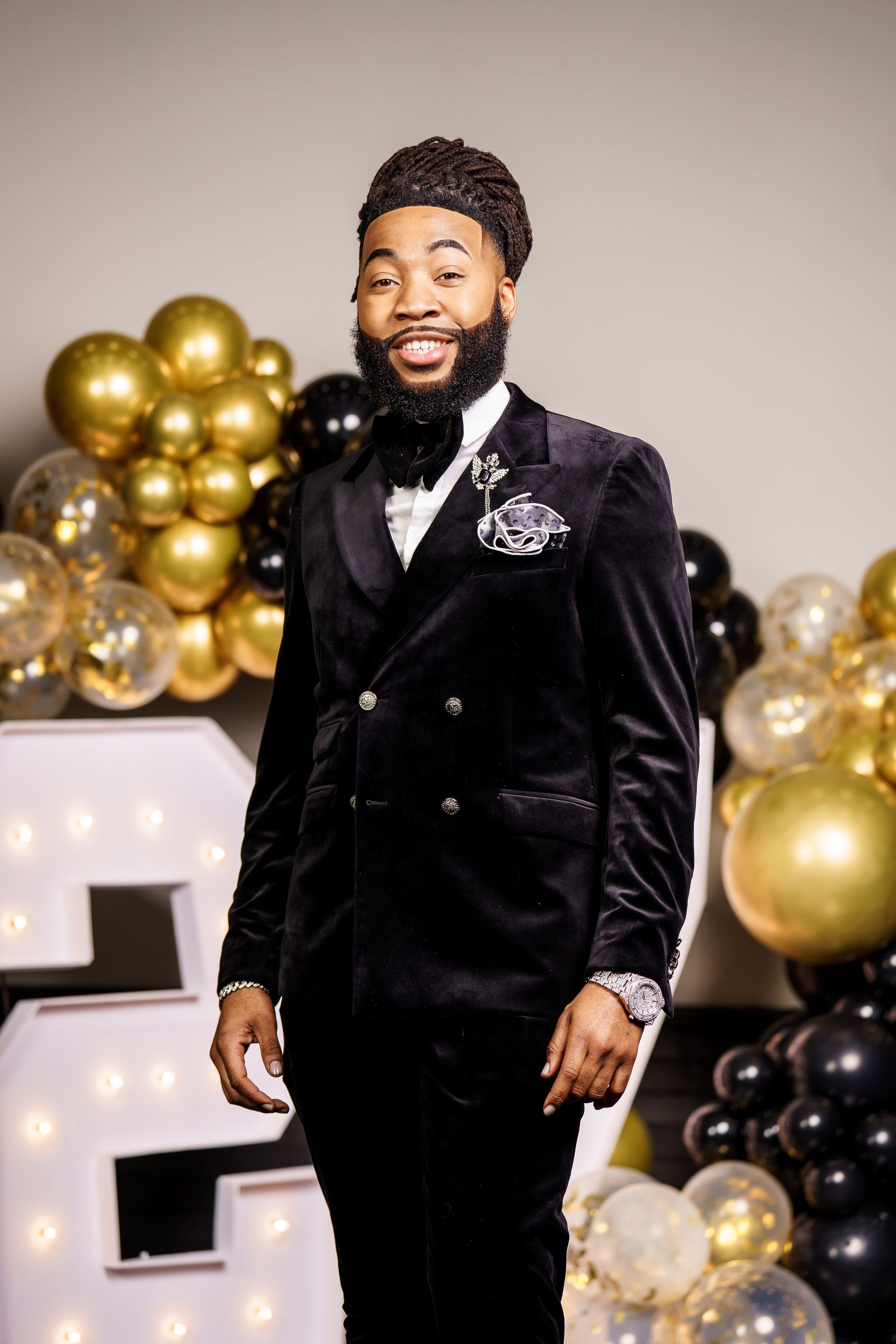 A man in a black suit and bow tie is standing in front of balloons.