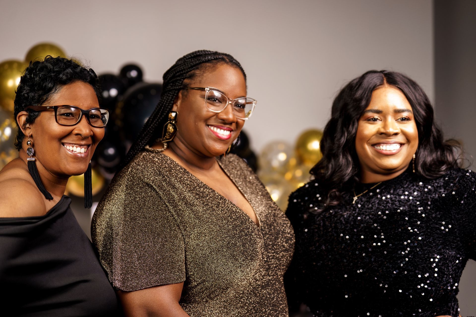 Three women are posing for a picture together in front of balloons.