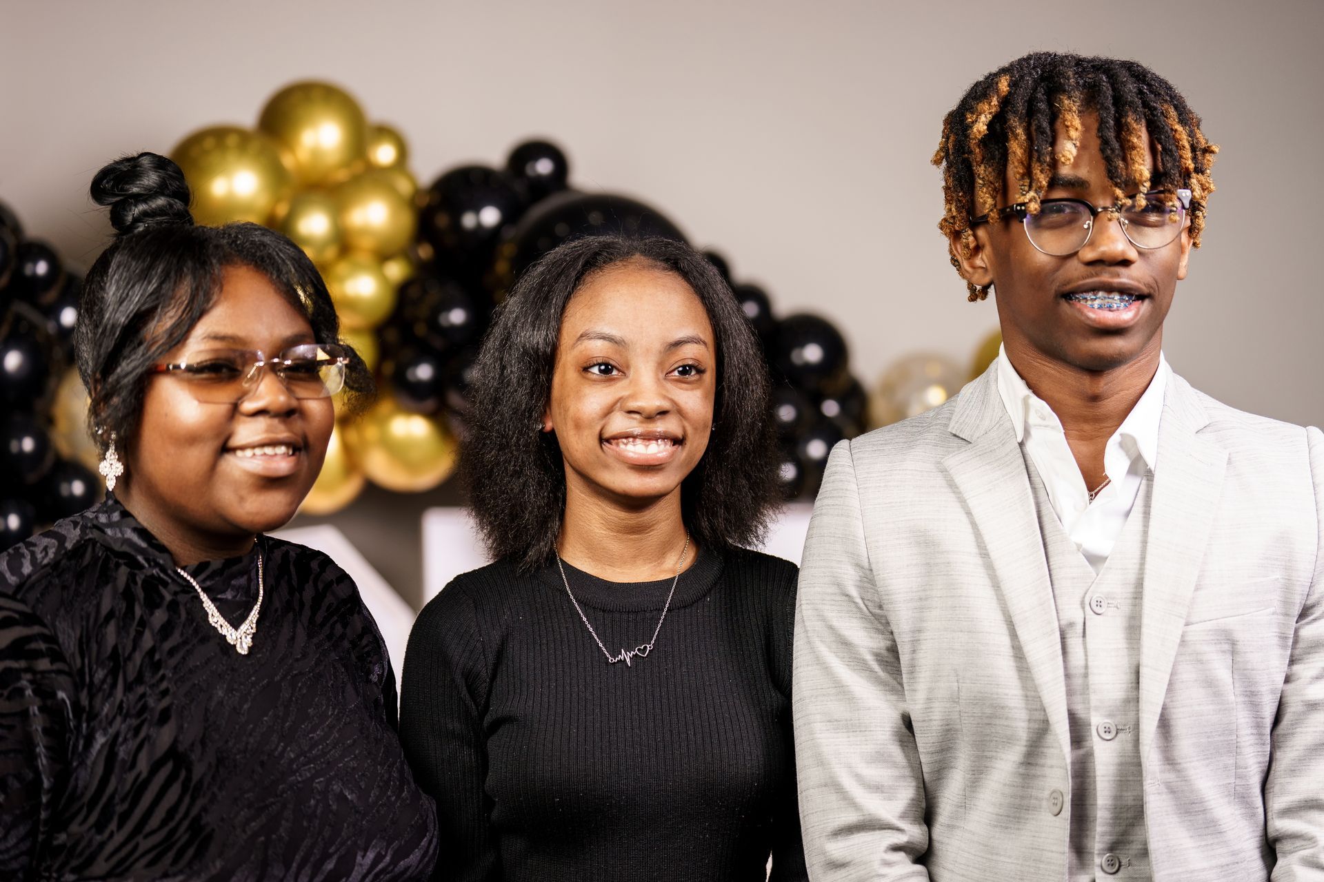 A man and two women are posing for a picture in front of balloons.