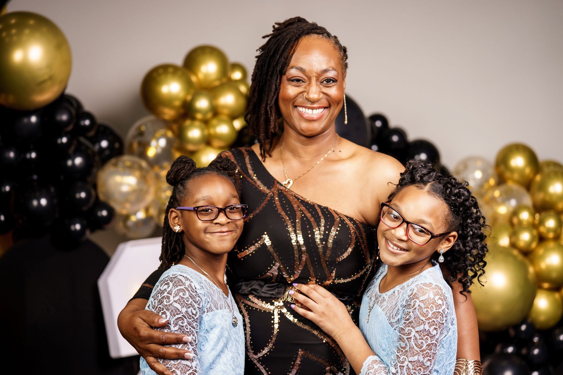 A woman is posing for a picture with two little girls in front of balloons.