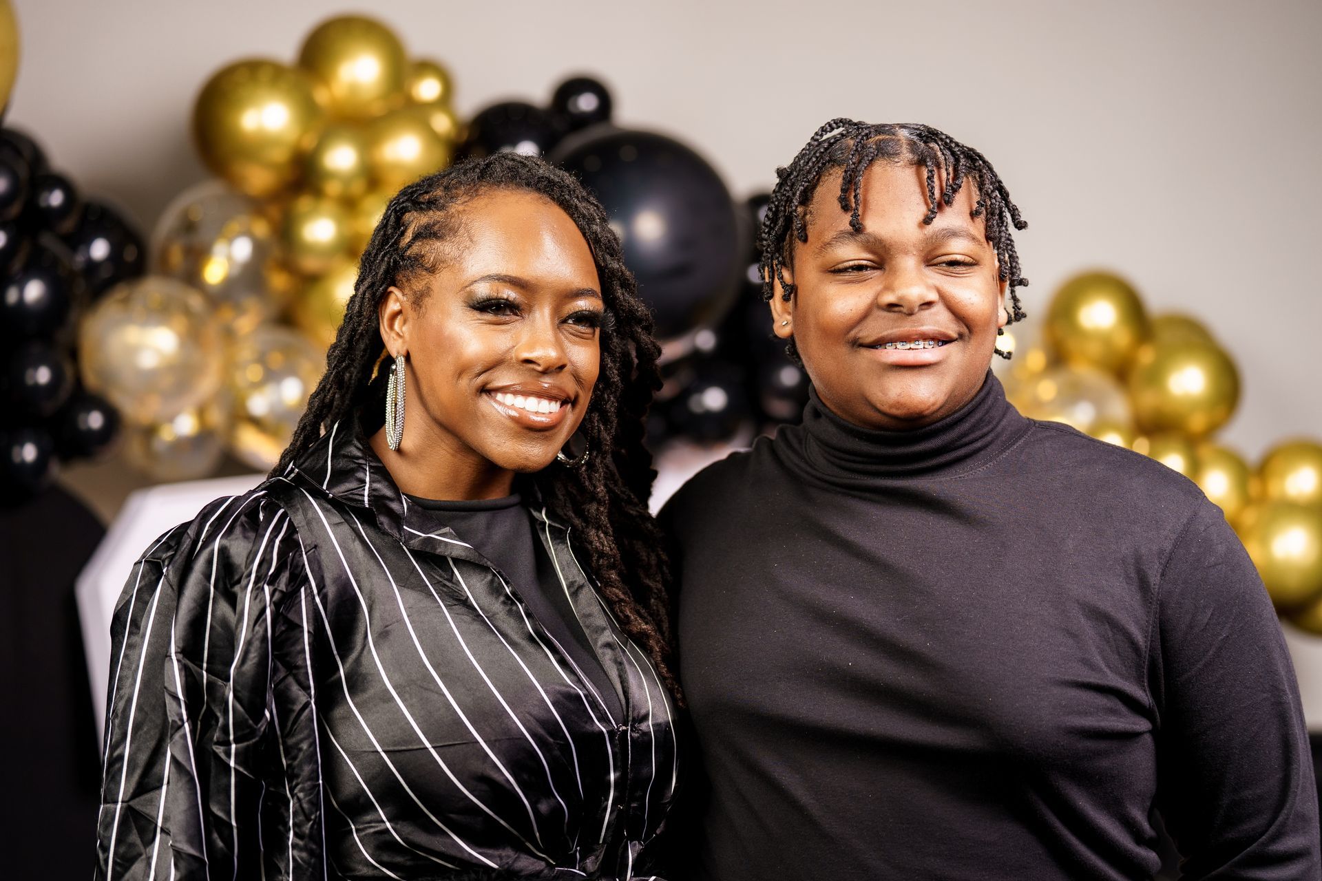 Two women are posing for a picture in front of balloons.