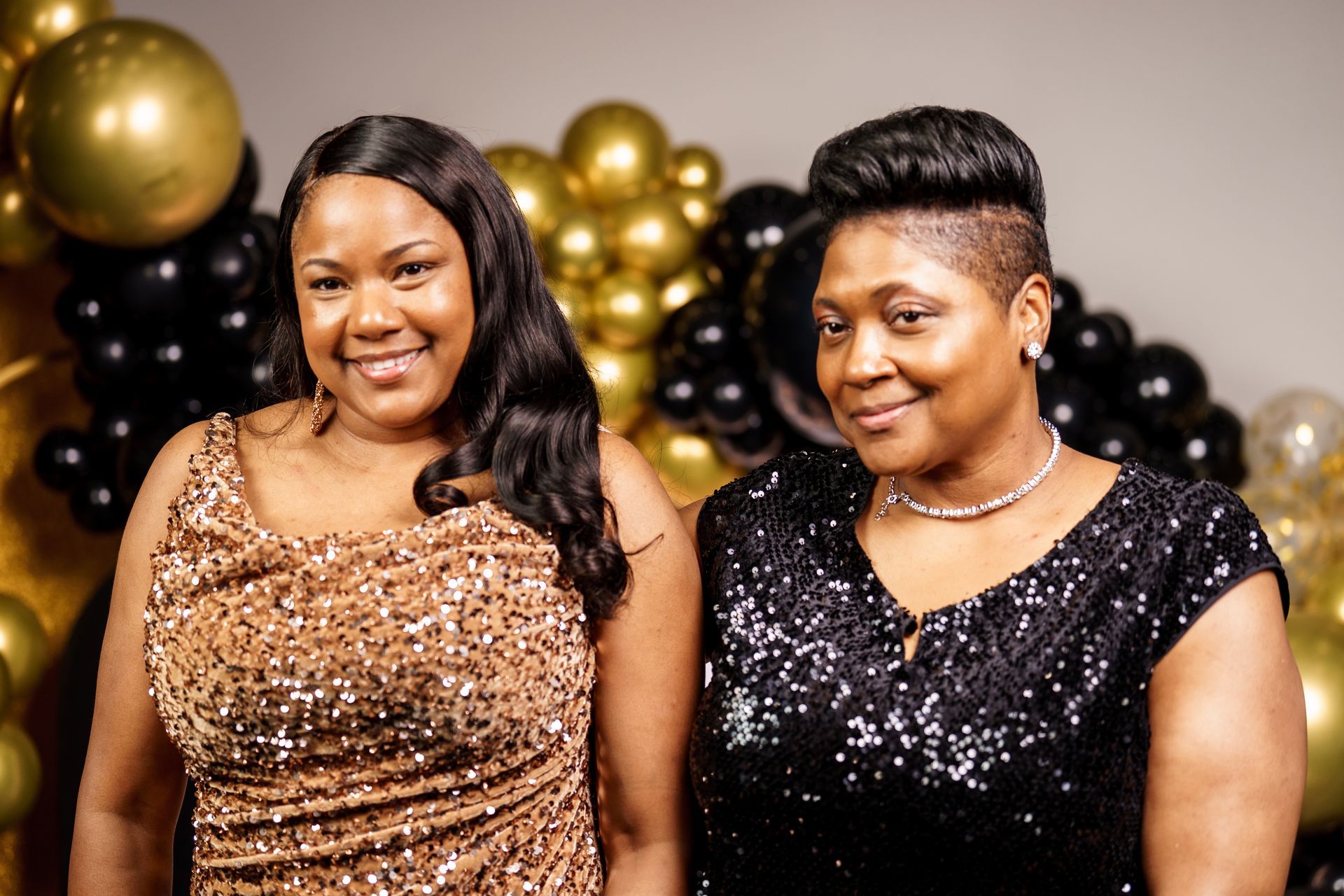 Two women are standing next to each other in front of balloons.