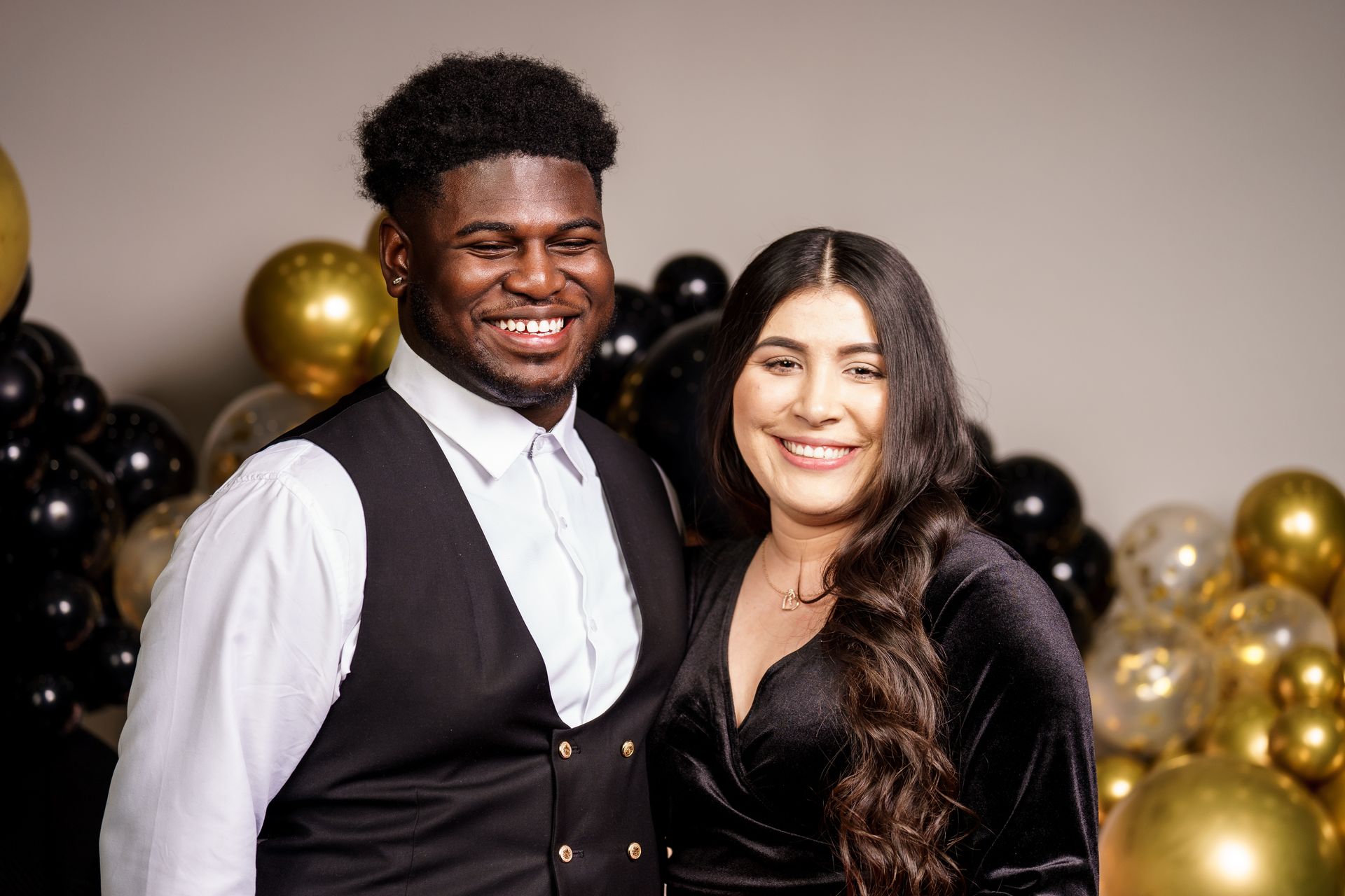 A man and a woman are posing for a picture in front of balloons.