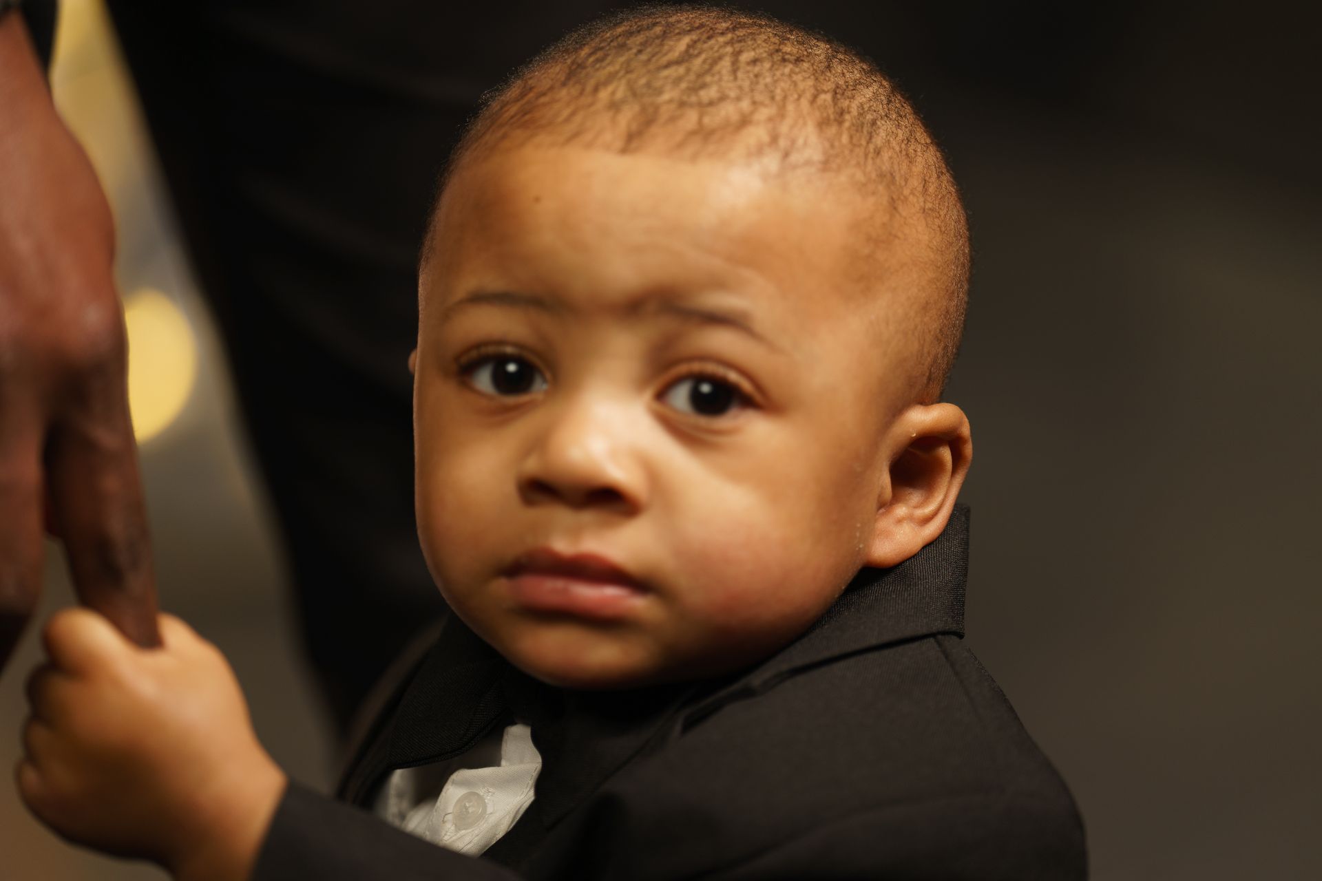 A little boy in a tuxedo is holding a man 's hand.