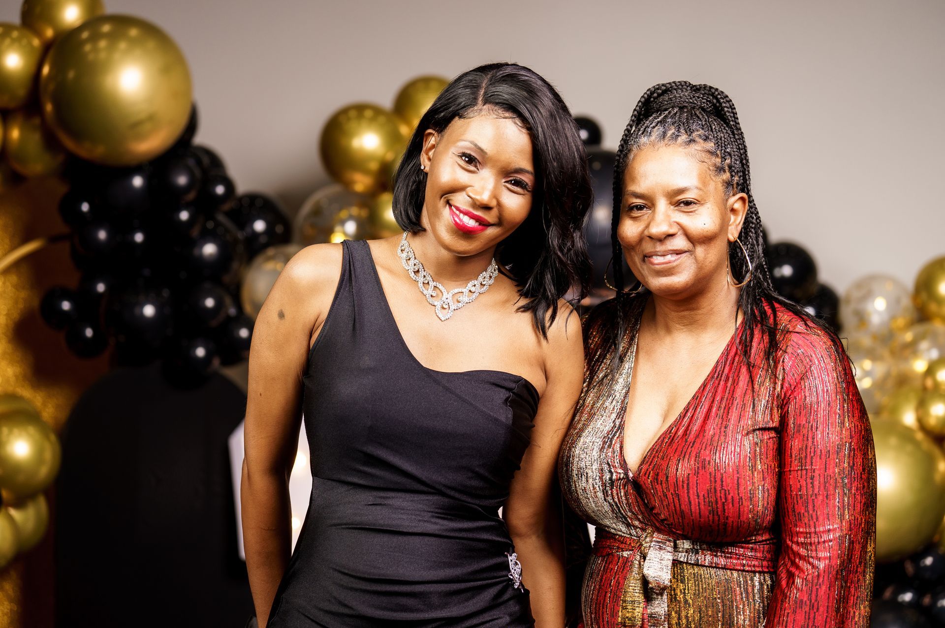 Two women are posing for a picture in front of balloons.