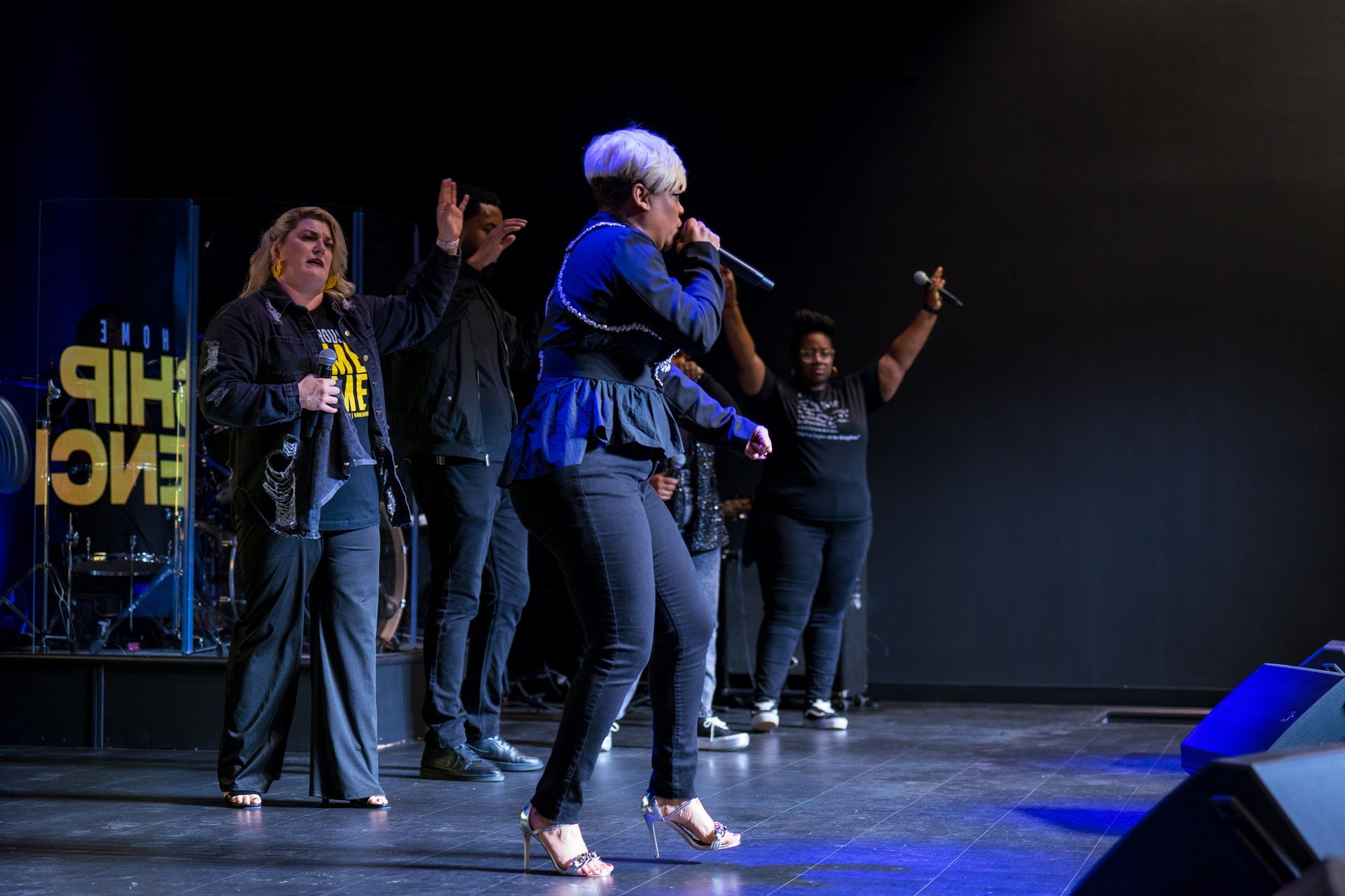 A group of people are standing on a stage singing into microphones.