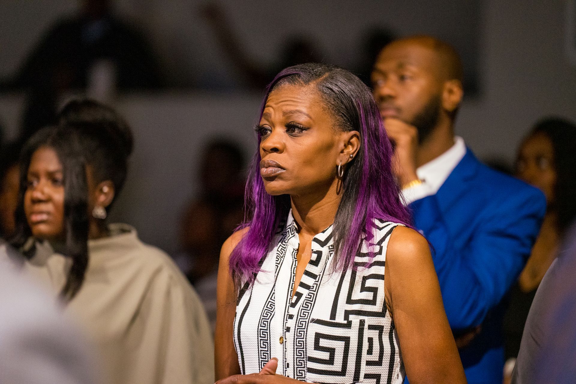 A woman with purple hair is standing in a crowd of people.