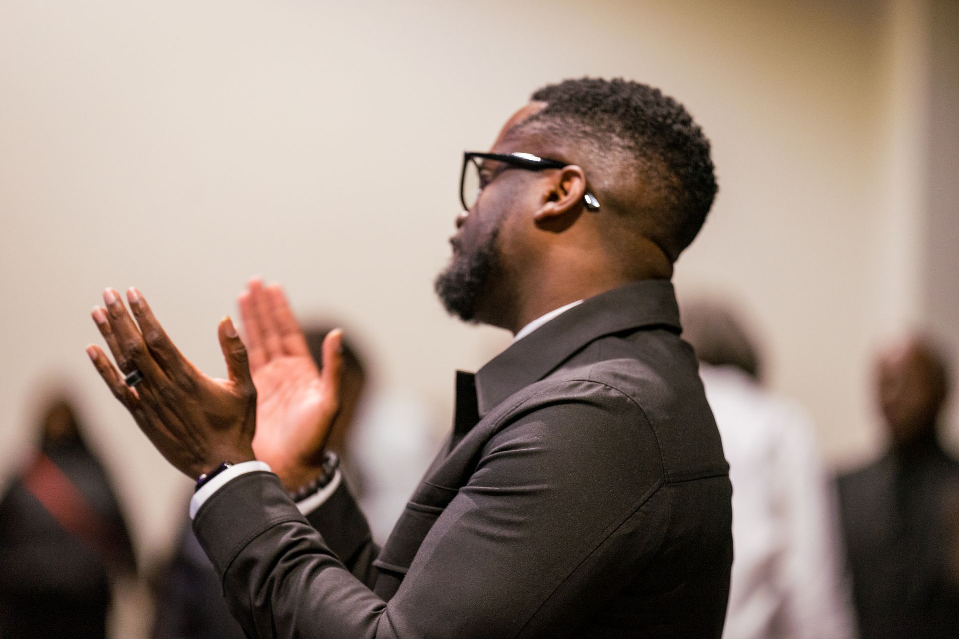 A man in a suit and glasses is clapping his hands.