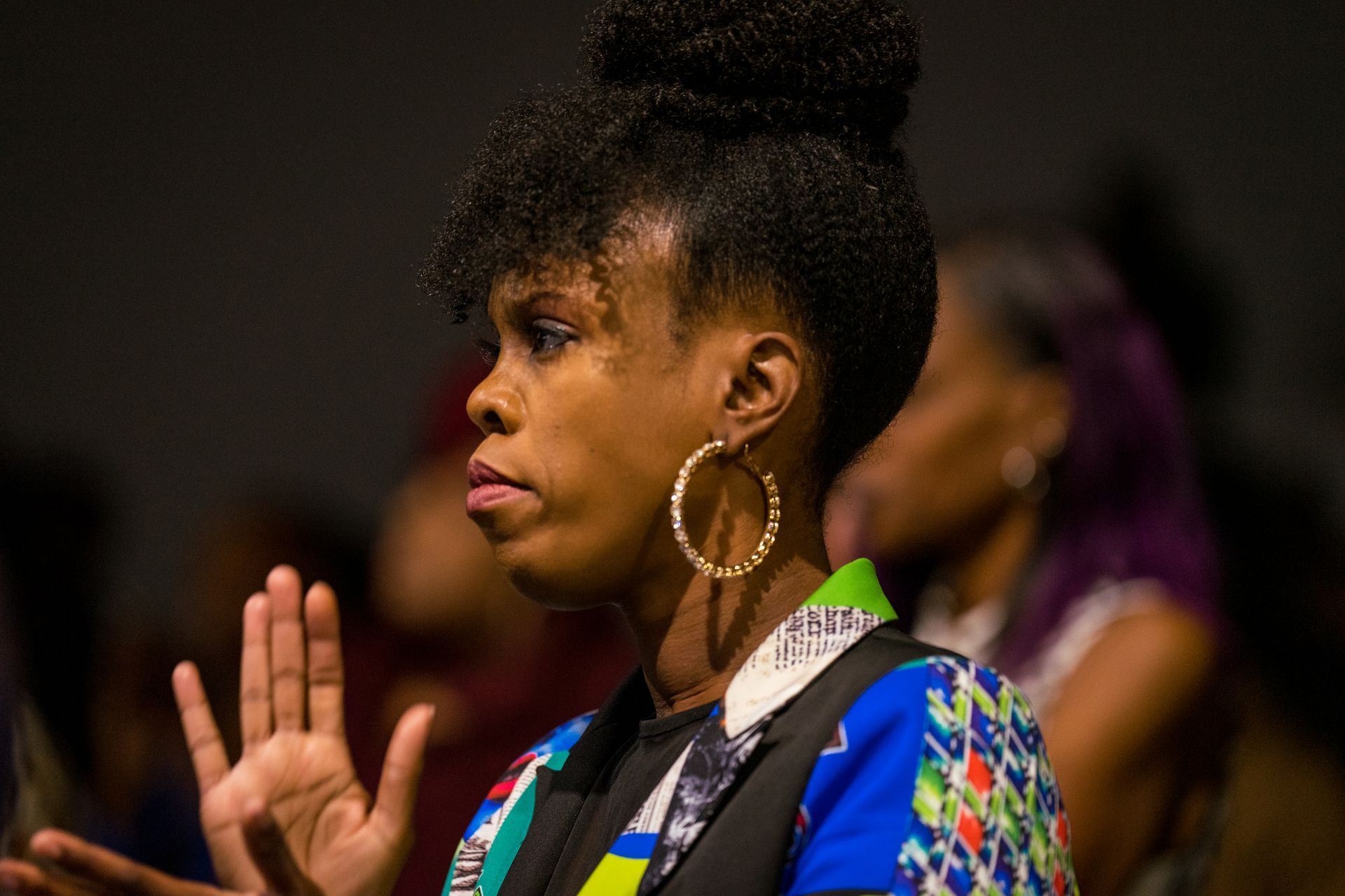 A woman wearing hoop earrings is sitting in a crowd of people.