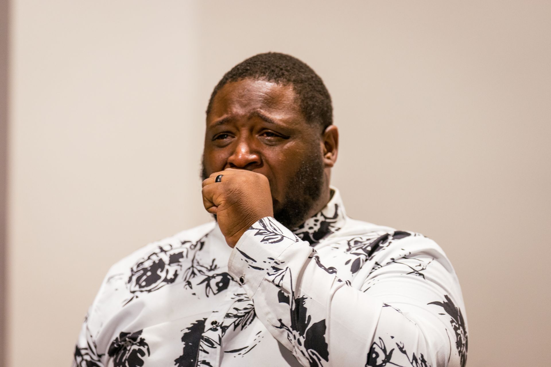 A man in a white shirt is covering his mouth with his hand.