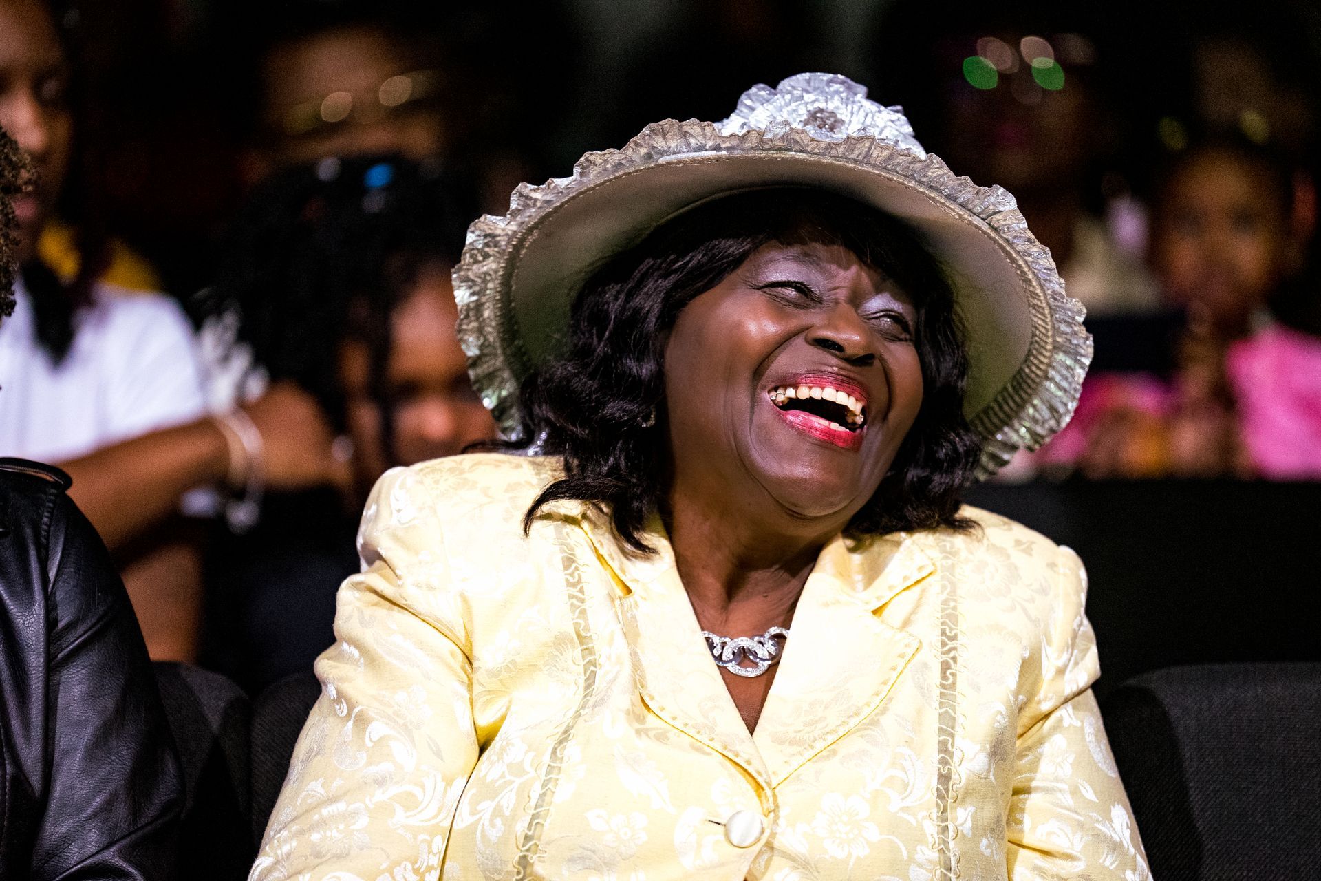 A woman wearing a hat and a yellow jacket is laughing.
