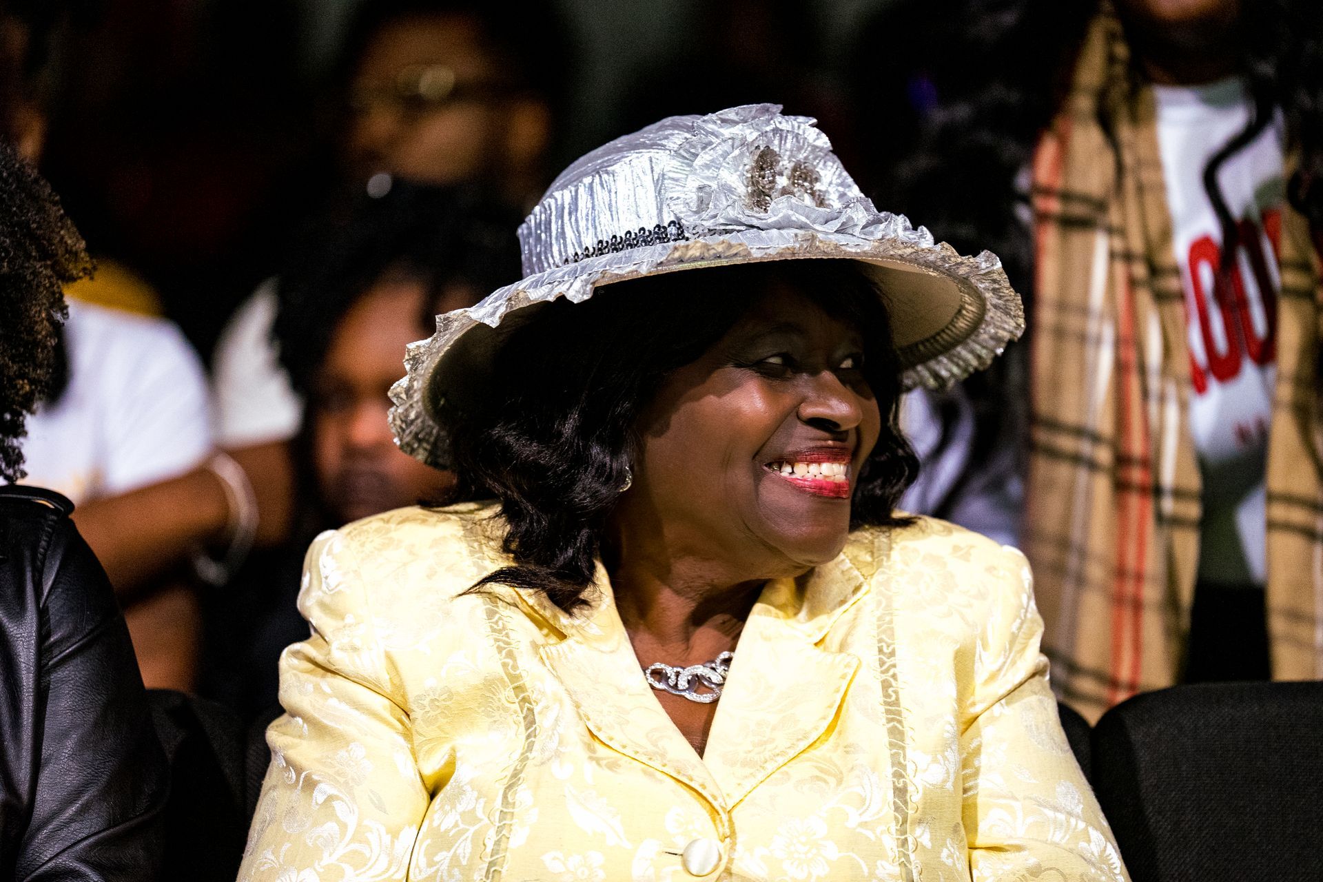A woman wearing a hat and a yellow jacket is smiling.