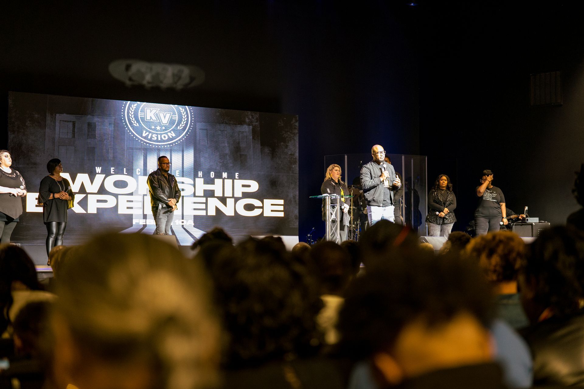 A group of people are standing on a stage in front of a large screen.