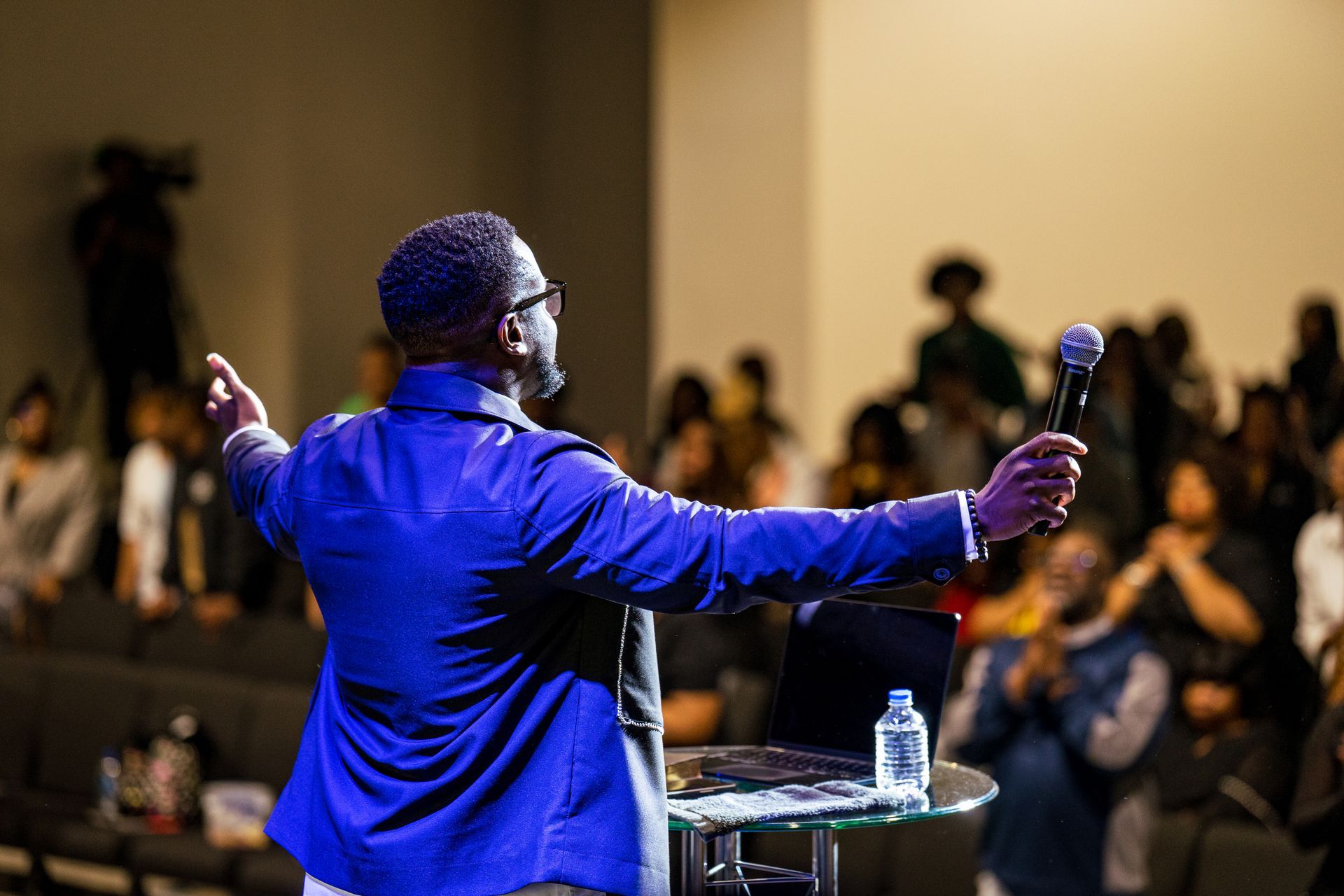 A man in a blue jacket is giving a speech in front of a crowd.