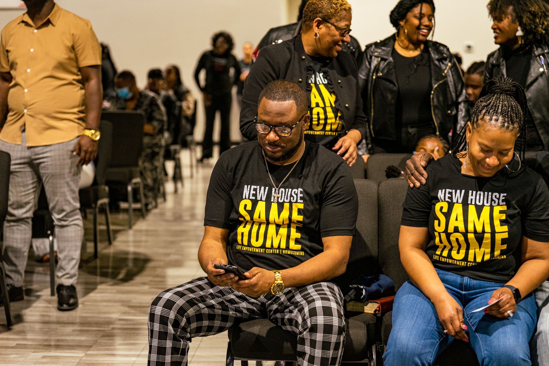 A group of people are sitting in chairs wearing t-shirts that say `` same home ''.