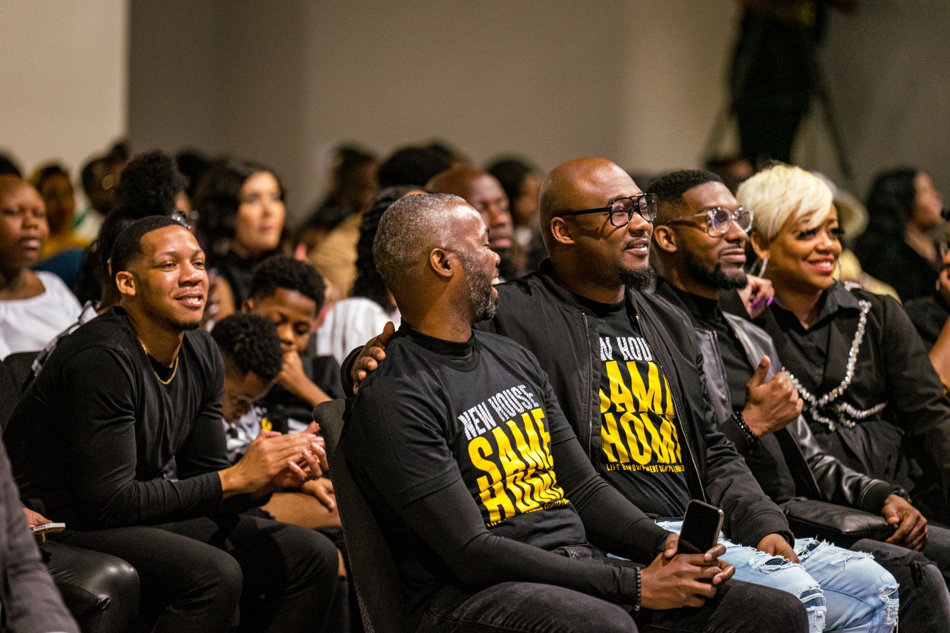 A group of people are sitting in a room wearing black shirts.