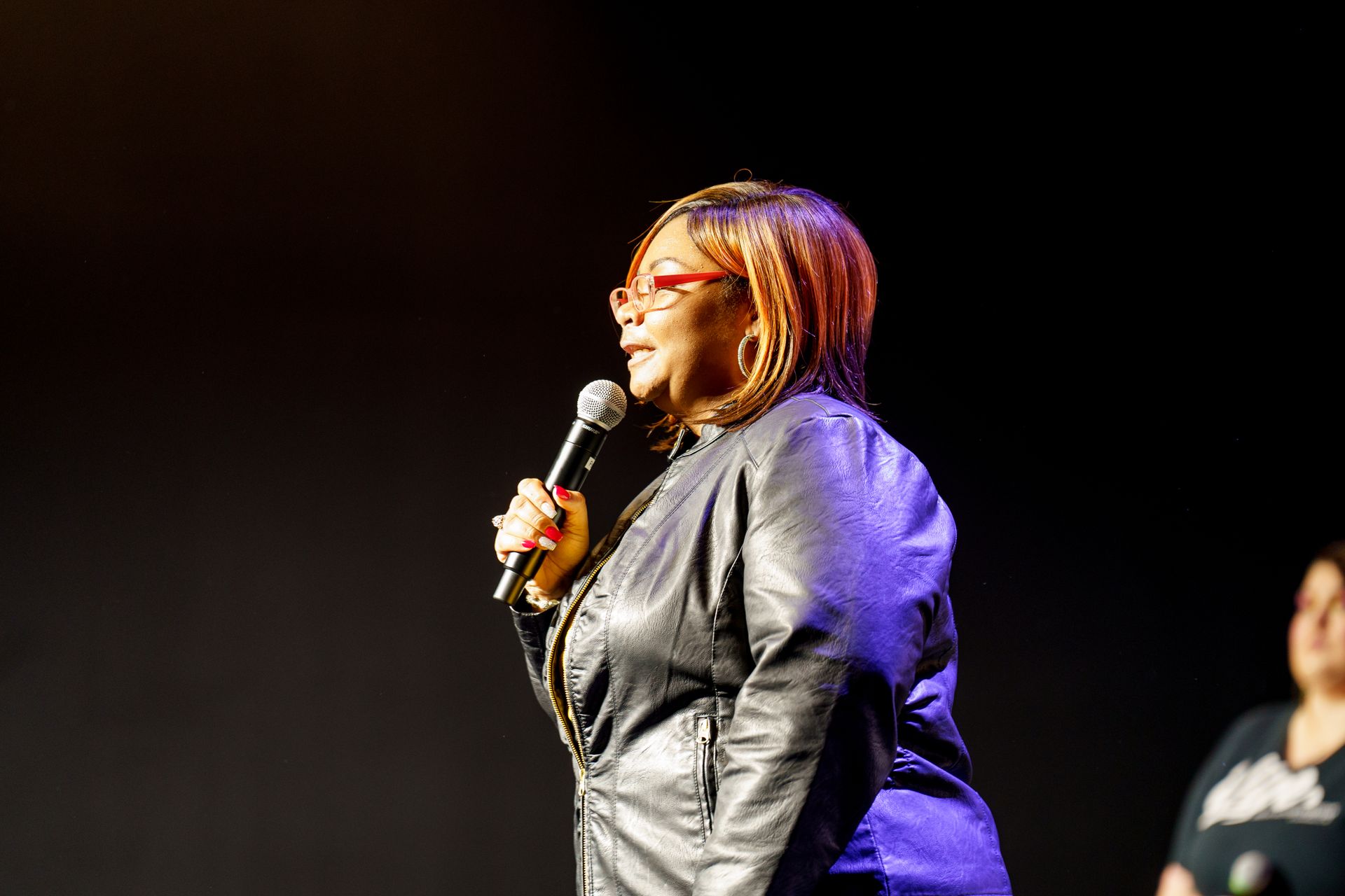 A woman in a leather jacket is singing into a microphone on a stage.