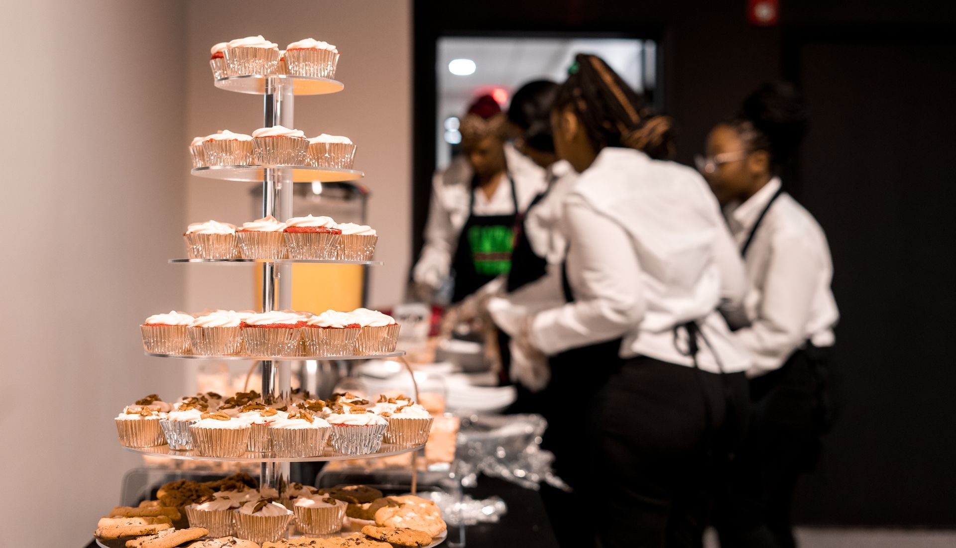 A group of people are standing around a table with cupcakes on it.