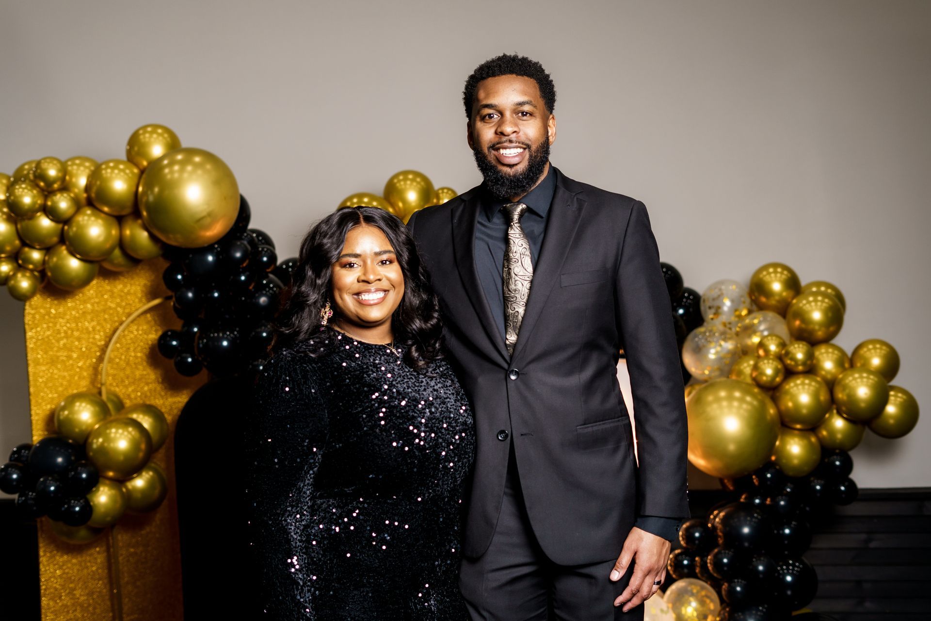 A man and a woman are posing for a picture in front of balloons.